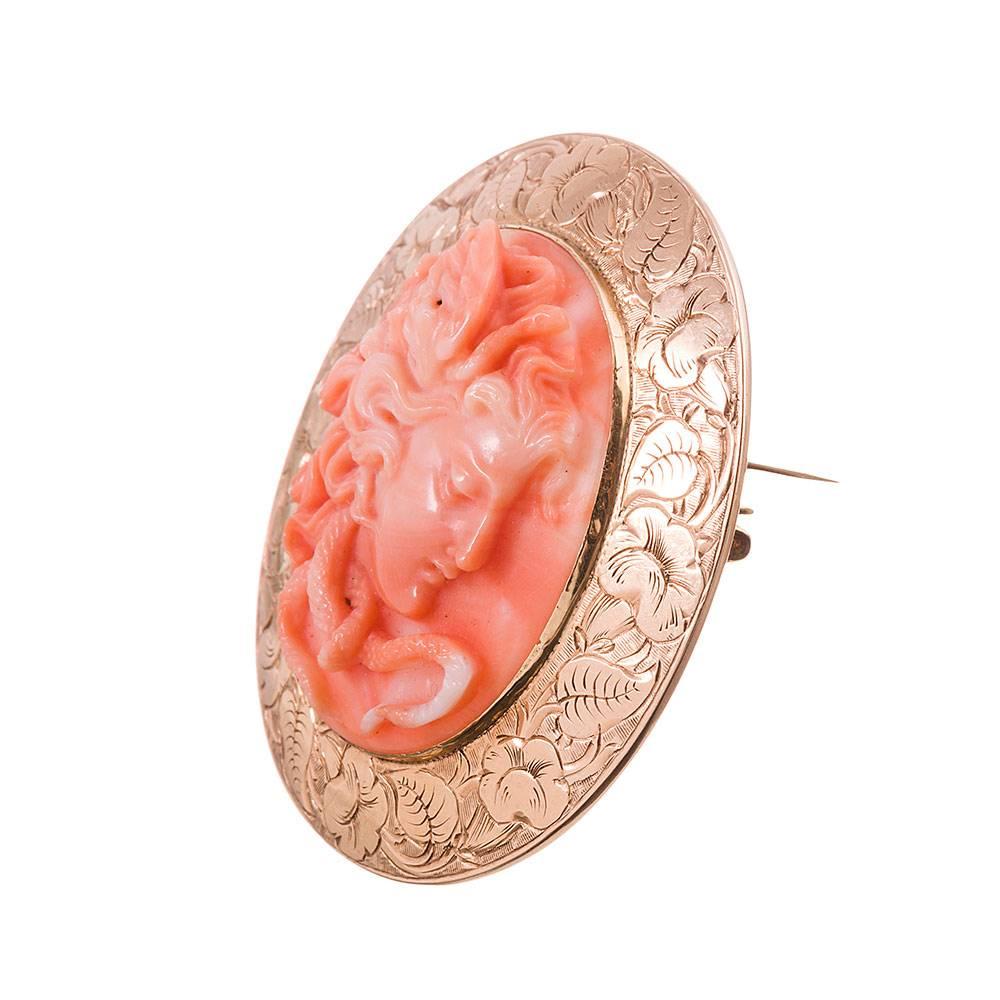 Medusa is carved of coral, her hair a wild ball of serpents, yet a peaceful expression on her face, and outlined in a golden frame of flowers and leaves. The 14 karat frame is fitted with a pin back. 2 by 1 3/4 inches. 