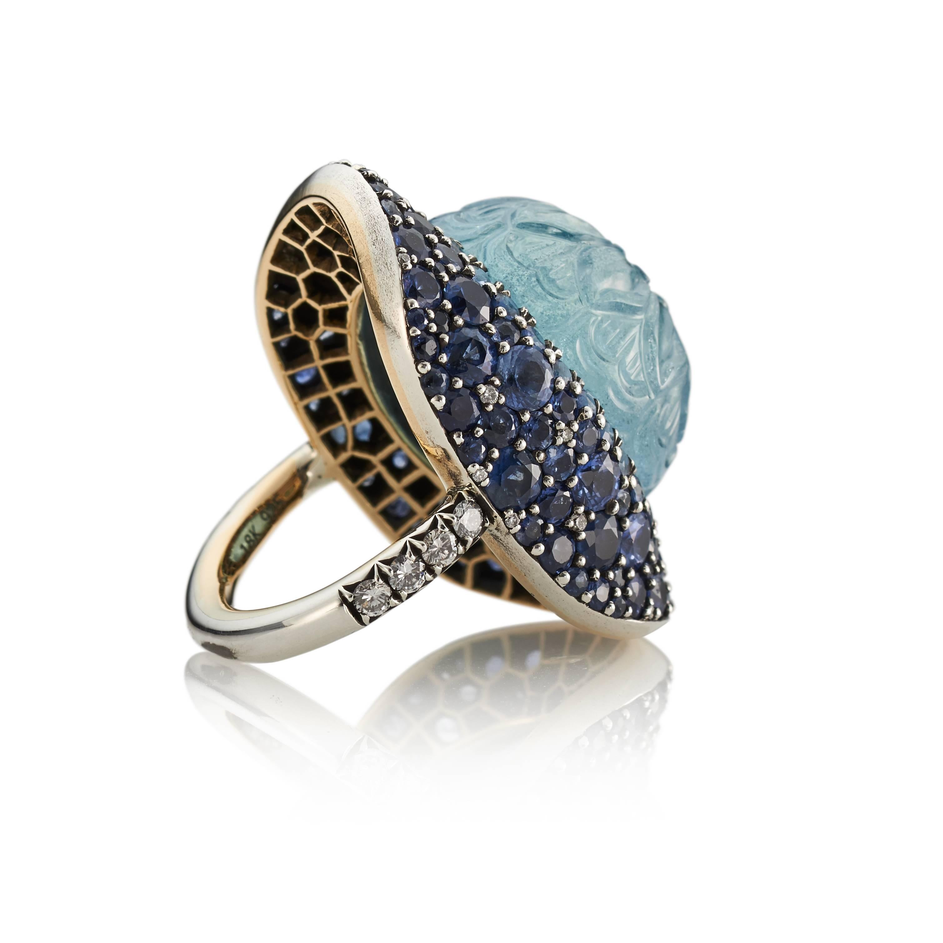 Look no further if you're seeking a truly distinctive and one-of-a-kind statement ring.  Showcasing a stunning 30.54 carat oval aquamarine that is hand-carved with a swirl floral motif, the gem is further accentuated with brilliant blue sapphires