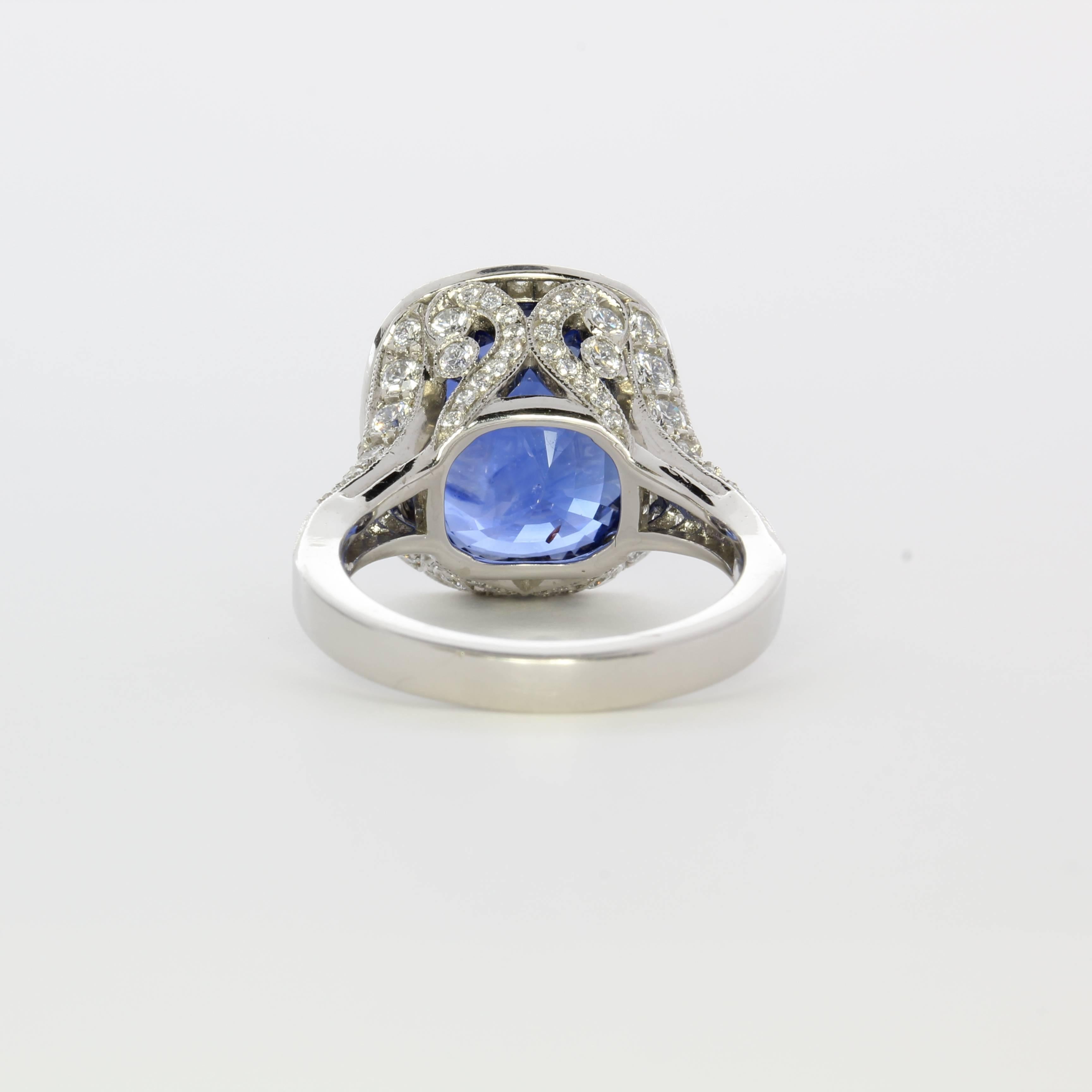 Natural sapphire from Madagascar, origin of the world’s finest gem sapphires.  Stunning handmade ring with unheated 12.41 carat cushion shaped sapphire, framed with 1.45 carats of diamonds, with square-cut and round diamonds on the band.   The