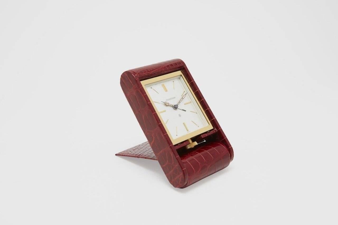 A gold plated and cherry red alligator wrapped Jaeger LeCoultre Ados travel clock. This is a spectacular example of a beautiful travel or desk clock in "New Old Stock" condition, including the original box. The clock was conceived by