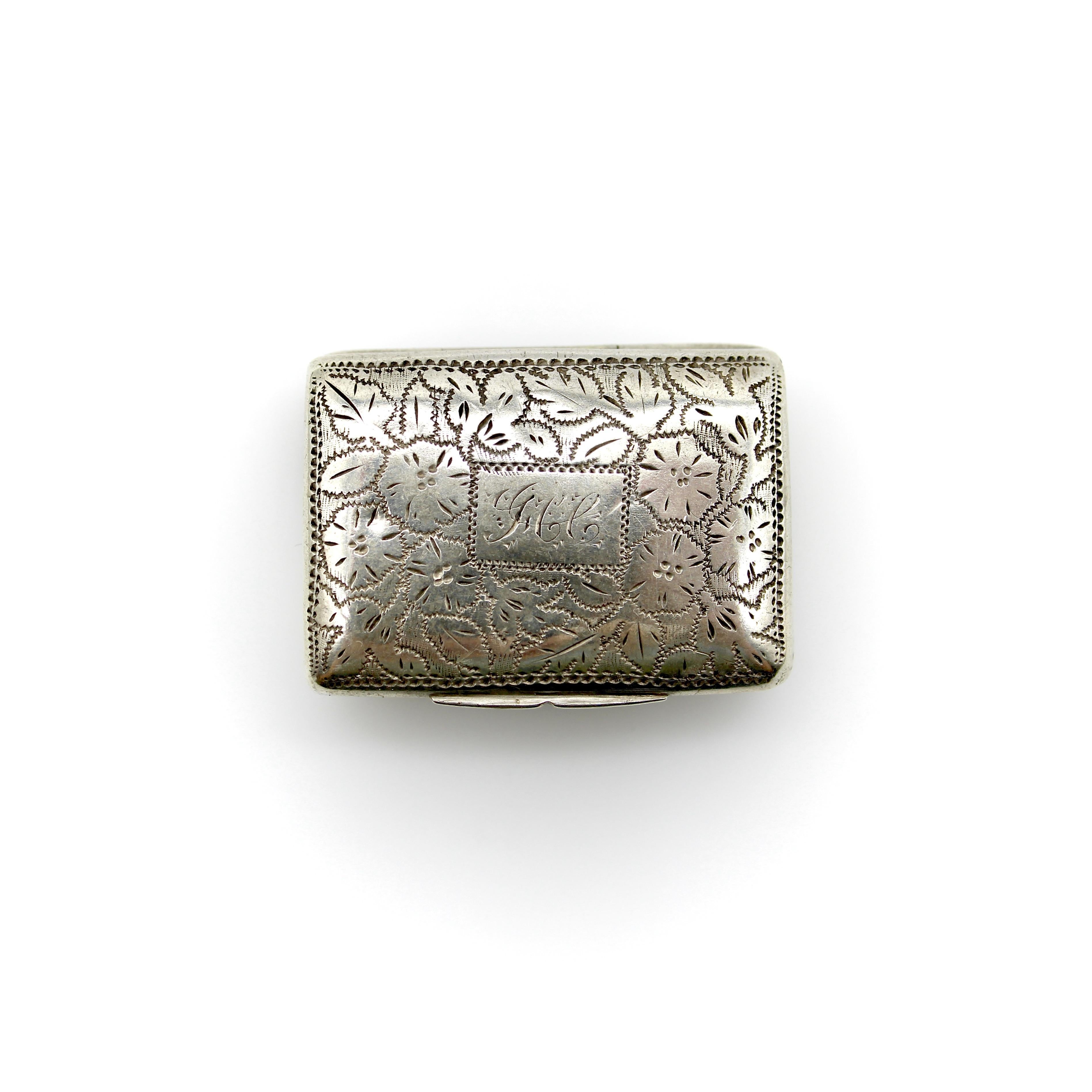 This sterling silver vinaigrette dates to the William IV era. It is engraved with a floral design and a sprigged script monogram at the center. The base has an acorn and oak leaf design that consists of tiny tick marks, with a scalloped border