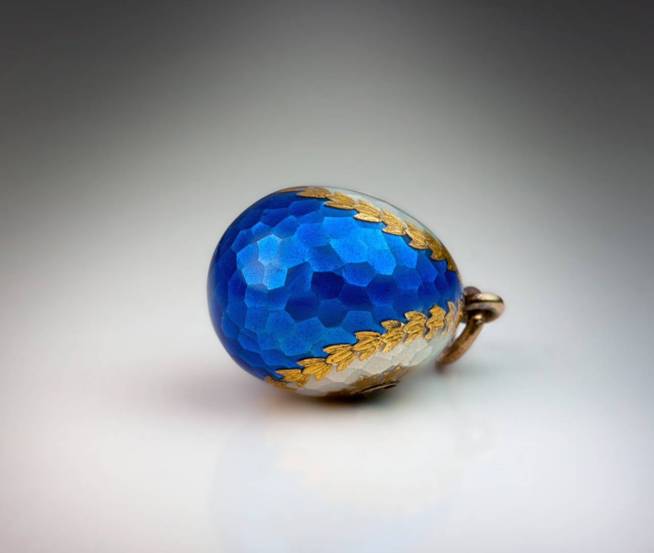 This very fine quality, elaborately decorated egg was made in Russia between 1899 and 1908. The surface texture of the egg is finished to resemble a hammered metal. The egg is covered with pearl white and royal blue translucent enamels separated