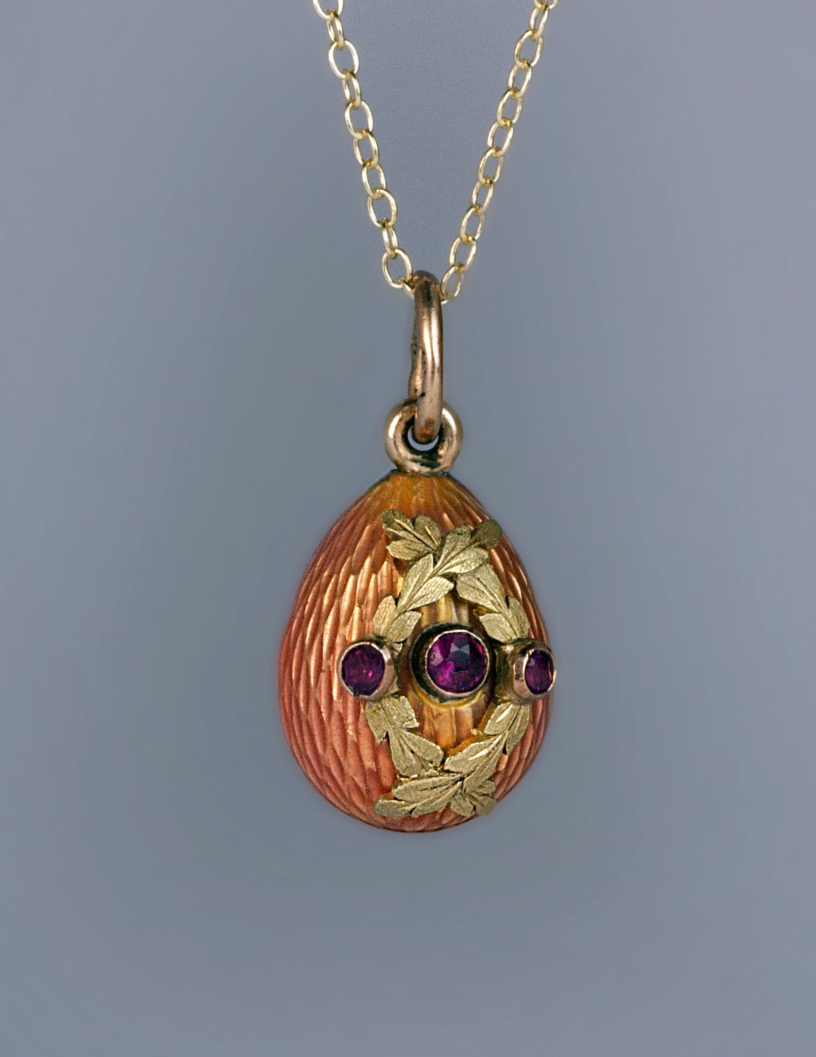 Made in St. Petersburg between 1899 and 1901. 

 The egg is covered with a salmon pink guilloche enamel. The front is centered with a bezel-set round faceted ruby flanked by two overlapping chased green gold garlands, each set with a small ruby.