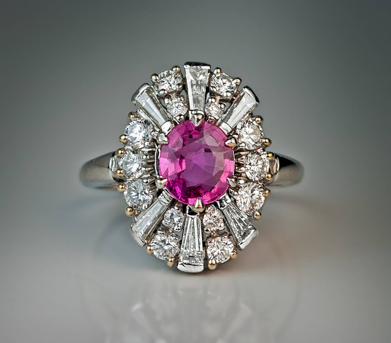 mid 1900s

 The ring is centered with a pink sapphire (7.2 x 6.3 x 3.2 mm, approximately 1.16 ct)vframed by round brilliant diamonds and tapered baguette diamonds.
The outer row of round diamonds is set in gold tipped platinum prongs. 