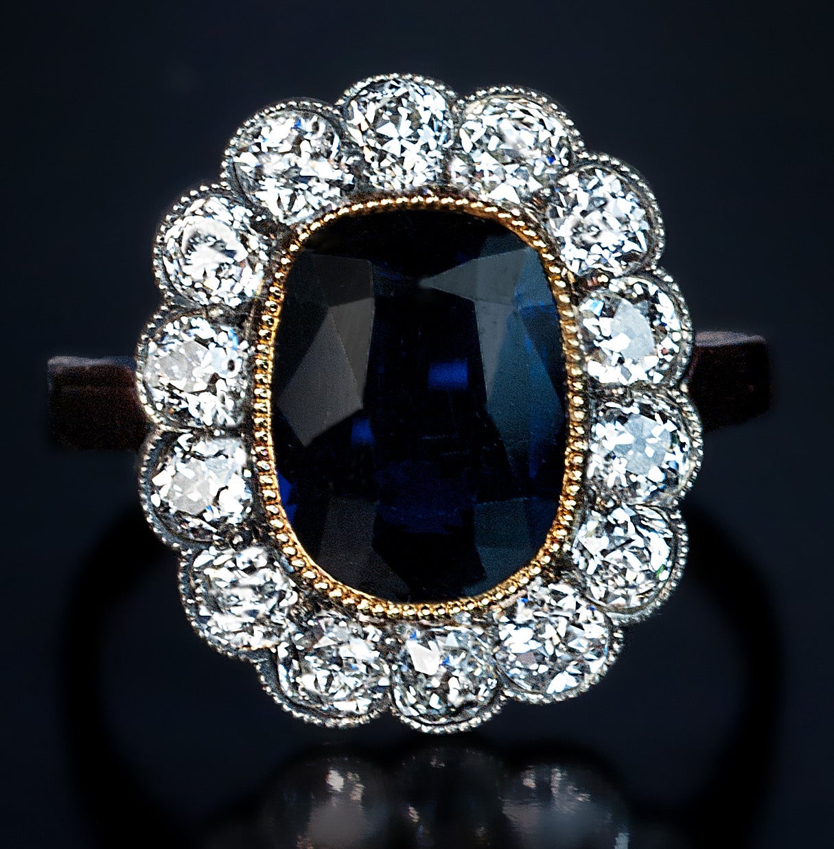 Russian, circa 1910

The 14K gold cluster ring is centered with a cushion cut sapphire (9.8 x 7.4 x 3.6 mm, approximately 2.02 ct) set in a milgrain gold bezel surrounded by 14 old European cut diamonds (estimated total diamond weight 1.40 ct) set