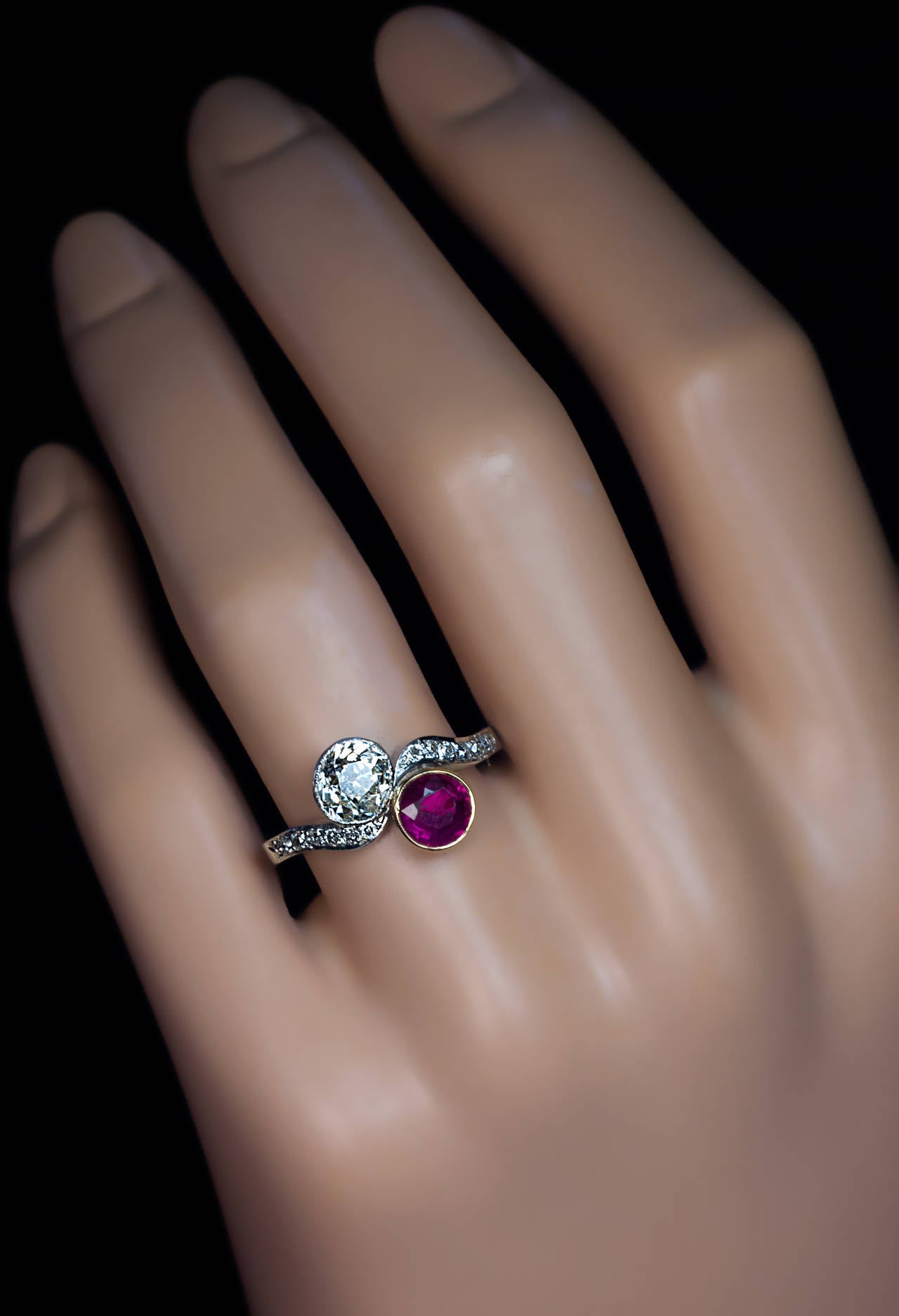 1920s / 1930s

A platinum bypass / moi et toi engagement ring centered with a round faceted ruby (5.8 x 2.9 mm, approximately 0.70 ct) and an old cushion cut diamond (6 x 5.4 x 3.95 mm, approximately 1.15 ct), shoulders set with 14 old European