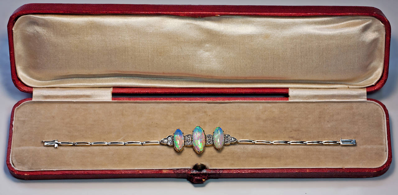 circa 1910

The silver topped gold bracelet is centered with three elongated oval opals which display a vibrant color palette: neon green, peacock blue and fluorescent purple with splashes of pink and orange. The opals are flanked by four