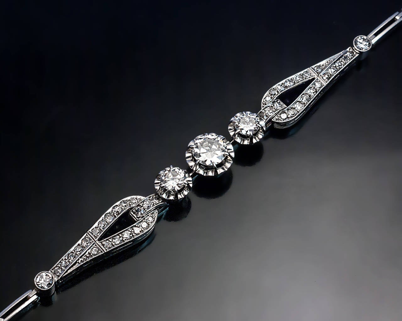 An elegant Art Deco diamond and platinum bracelet centered with three buttercup-set transitional brilliant cut diamonds flanked by two elongated drop-shaped links set with numerous single cut diamonds

Center diamond 5.85 x 5.9 x 2.8 mm