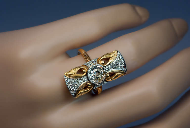 Circa 1900
This unique 18K yellow gold antique ring is designed as a stylized diamond-set platinum Maltese cross flanked by four chased gold openwork floral designs in the Art Nouveau style of the 1890s – early 1900s.
The ring features a champagne