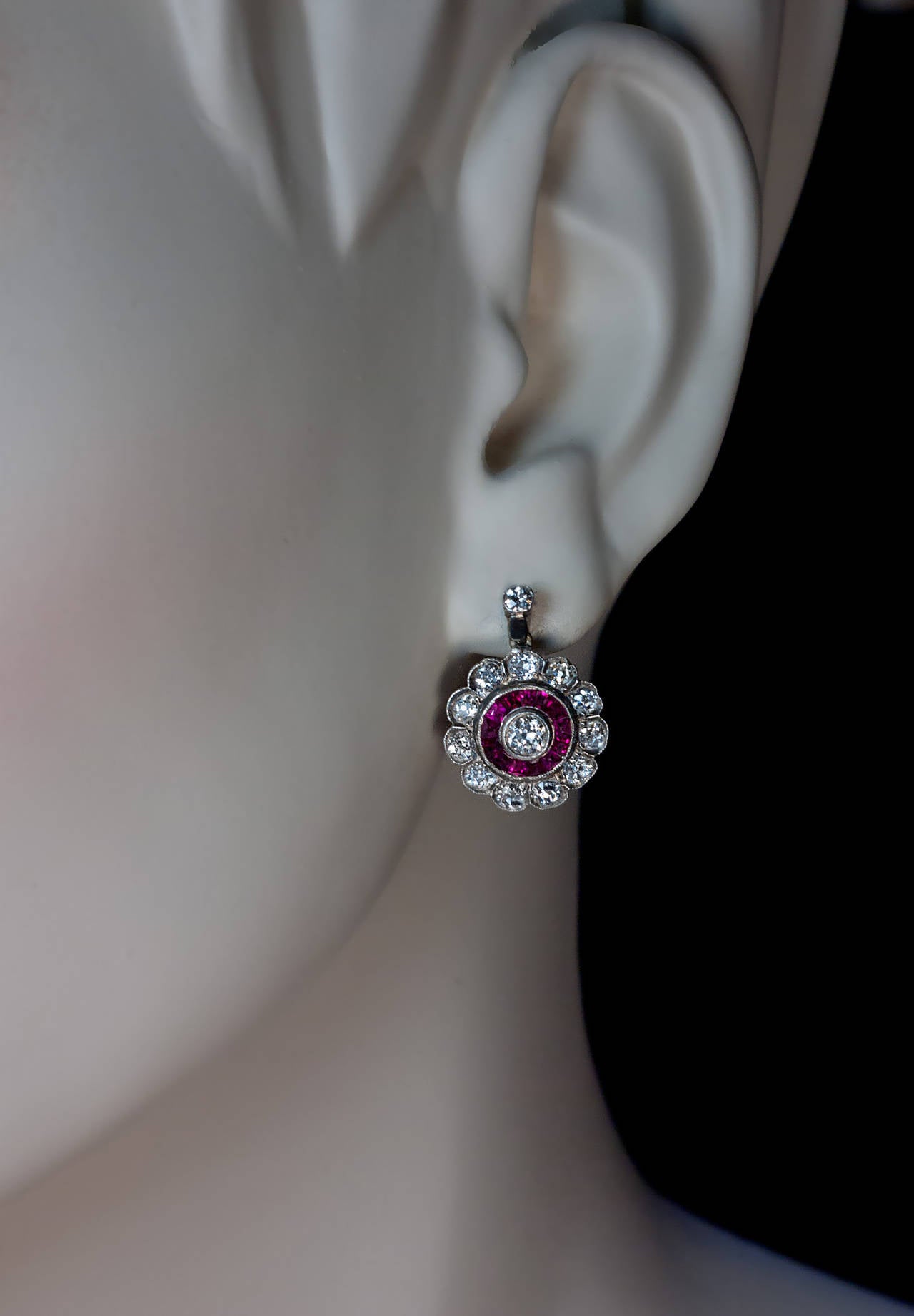 The earrings are crafted in silver topped 18K gold. 

The center diamonds (approximately 0.20 ct each) are surrounded by single rows of calibre cut channel-set synthetic rubies, in turn outlined by diamond-set petals. 

The diamonds are mostly