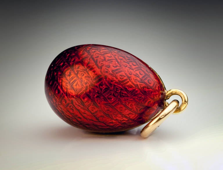 Made in Odessa between 1908 and 1917.

The egg is covered with superb deep strawberry red translucent enamel over an elaborate guiilloche design, the front centered with a tiny rose cut diamond.

Marked with 56 zolotnik gold standard (14K).