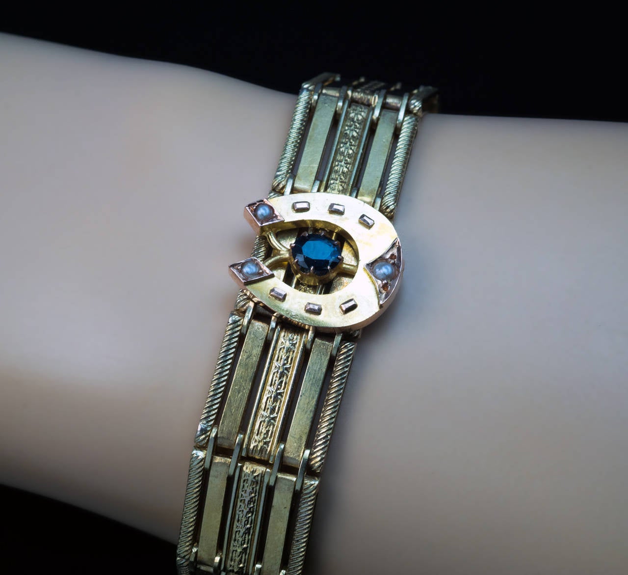 Made in Moscow between 1908 and 1917

The 14K gold link bracelet is mounted in the center with a stylized gold horseshoe embellished with a blue sapphire and three seed pearls. A small gold heart-shaped charm is attached to the clasp
Marked with
