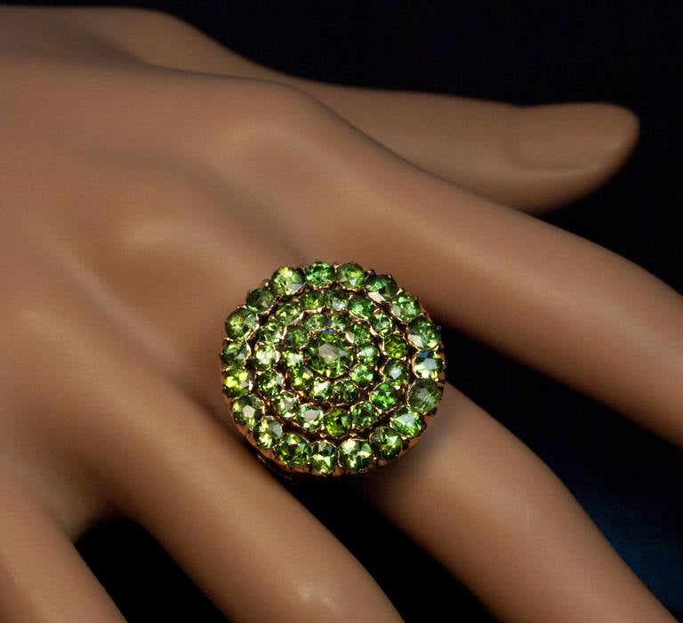 The top with 45 prong-set demantoids is circa 1900. The 14K rose gold shank is a later replacement. The ring is centered with an old cushion cut demantoid (approximately 0.56 ct) surrounded by three rows (10/15/19 stones) of mostly round sparkling