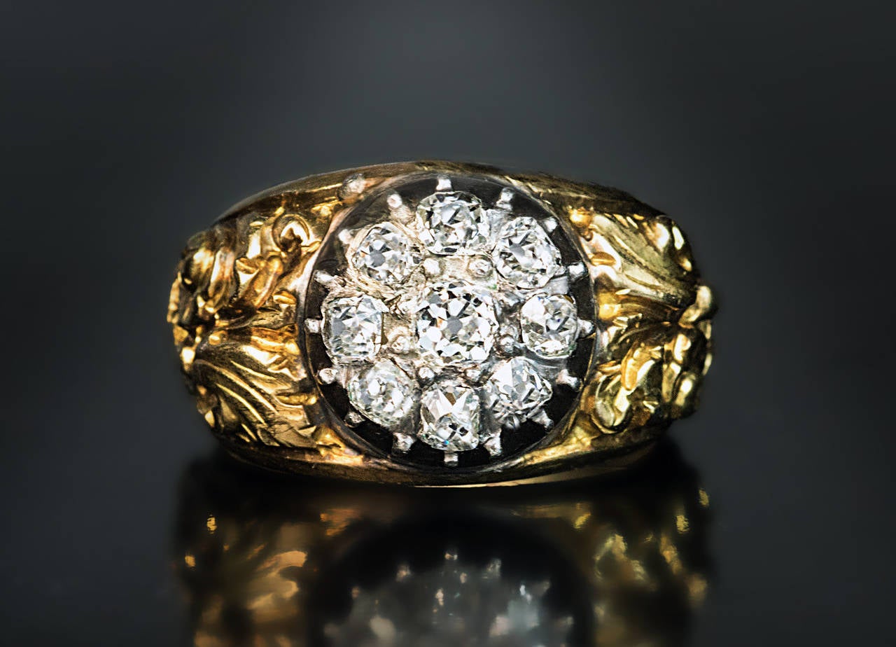 circa 1830

The 18K yellow gold ring is chased in high relief with a scrolling foliage 
and centered with a cluster of nine sparkling old cushion cut diamonds set in a silver setting.

Estimated total diamond weight 1.30 ct

Width 13 mm (1/2