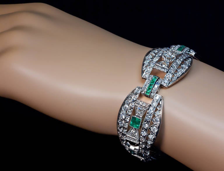 A bow themed saw-pierced platinum 23 mm wide bracelet embellished with emeralds and diamonds, the center plaque features a prong-set old European cut diamond - approximately 1 carat, I color, VS2 clarity

Estimated total diamond weight  12