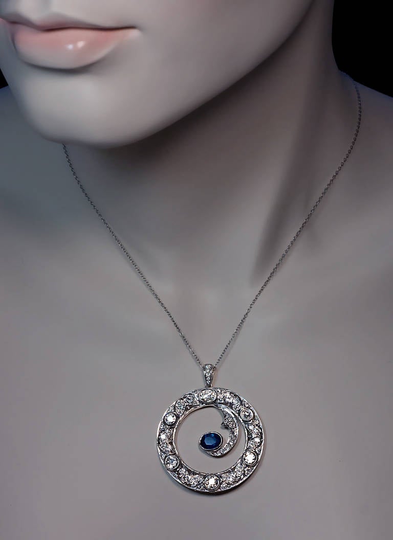 Circa 1930

 An openwork pendant handcrafted in white 18K gold, set with a natural blue sapphire and numerous old, transitional and modern cut diamonds

The sapphire - 7.4 x 5.5 x 3.35 mm, approximately 1.20 ct

The largest diamond - 5.7 x 4.3