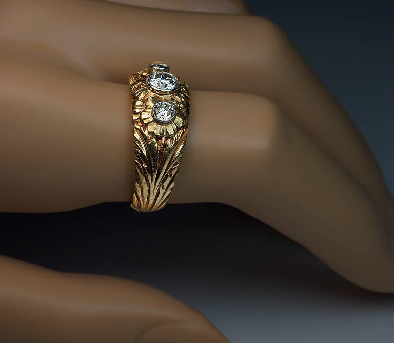 A heavy 18K yellow gold ring with superbly carved floral designs in Art Nouveau taste set with three brilliant diamonds (approximately 0.50 ct, 0.14 ct and 0.12 ct) in milgrain platinum bezels

weight 12.46 grams

width 11 mm (7/16 in.)

US