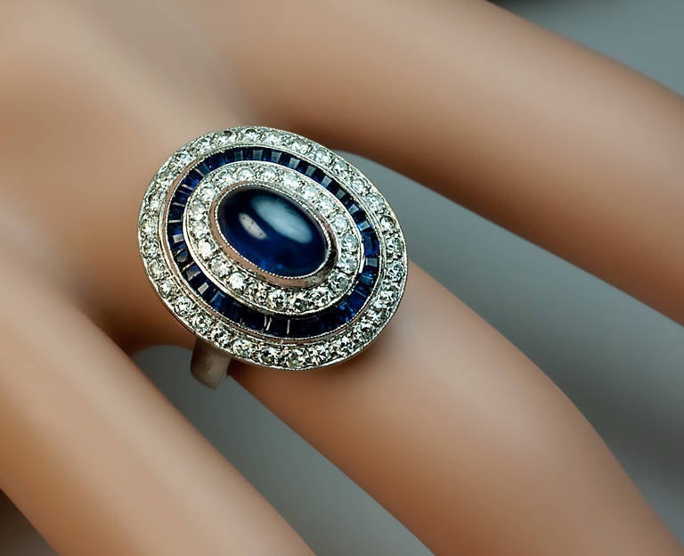 Belgium, 1940s

A handcrafted white gold ring is centered with a bezel-set cabochon cut sapphire encircled by two rows of brilliant diamonds and a row of calibre cut sapphires
Marked with maker's initials 'GA' and Belgian assay mark for 750 gold