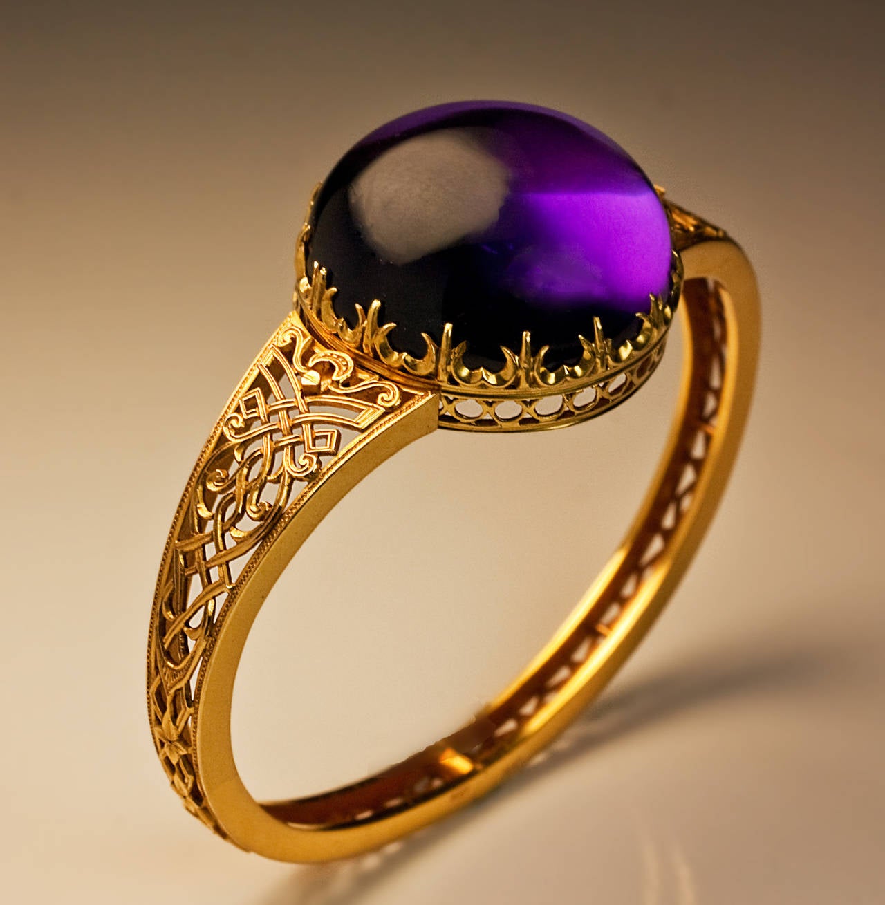 A 14K gold openwork hinged bracelet features a huge round cabochon cut amethyst (27.5 x 13.1 mm, approximately 70 carats) set in a crown like gold bezel.

The bracelet is decorated with an elaborate gold strapwork in medieval Gothic style. 

The
