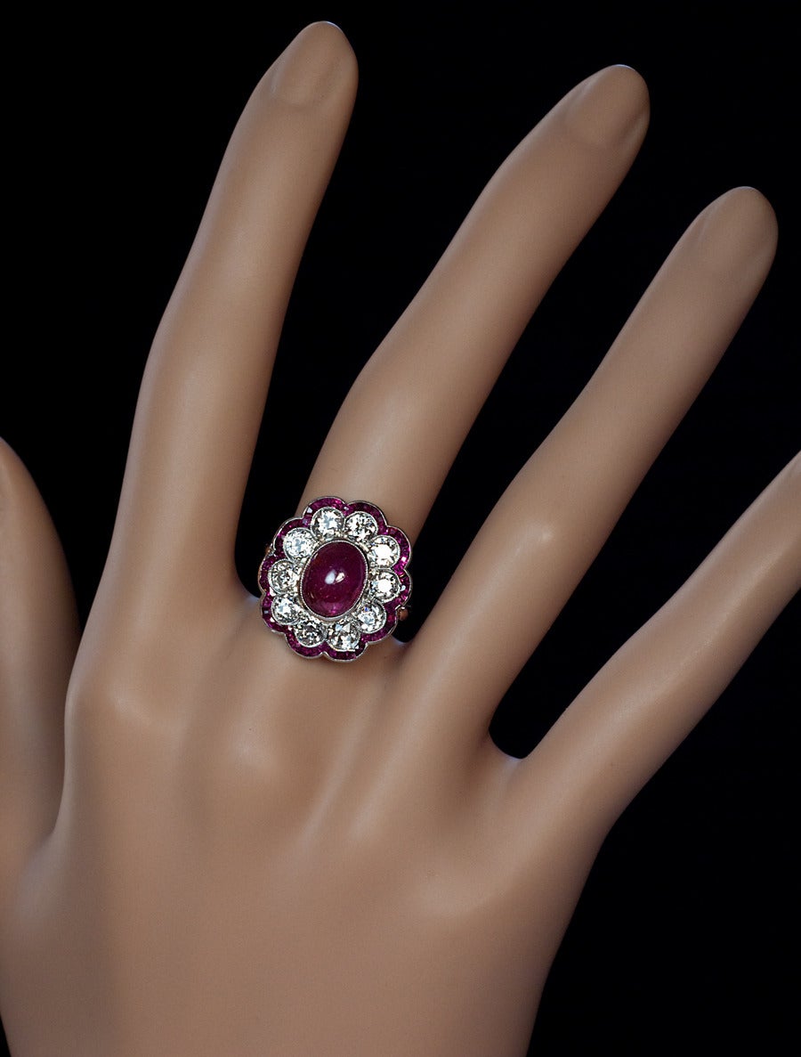 Circa 1910

This Edwardian era finely crafted fancy cluster ring features an oval cabochon cut natural untreated ruby (measuring 9.2 x 7.4 x 4.38 mm, approximately 3.22 ct) of Burmese origin. The center stone is framed by ten bright white and