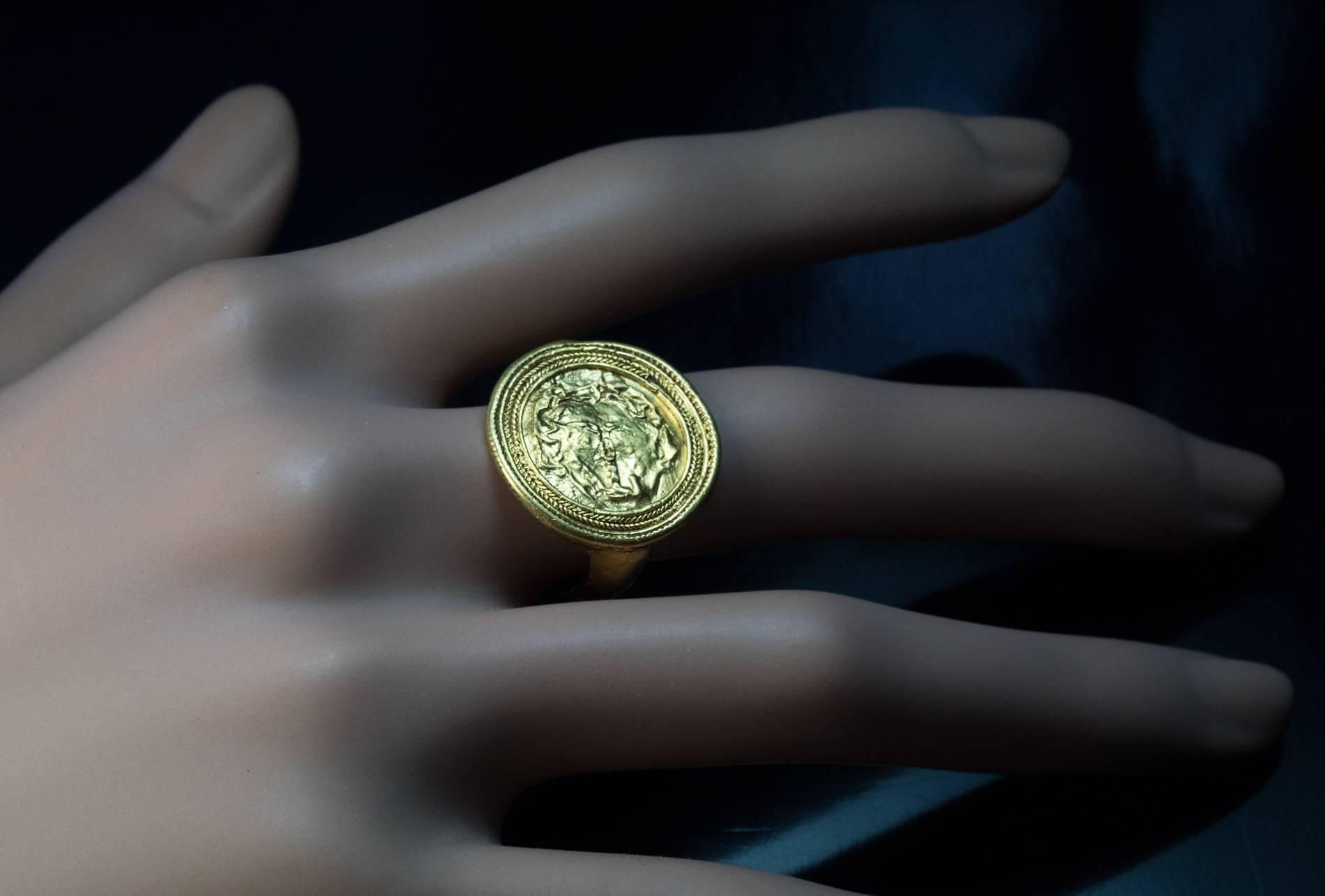 Antiker Kopf der Medusa Goldring

um 300 v. Chr.

Dieser Ring aus hochkarätigem hellenistischem Gold ist als Goldscheibe mit einer horizontal angeordneten archaischen Reliefbüste der Medusa gestaltet, die von zwei Reihen gedrehter Golddrähte