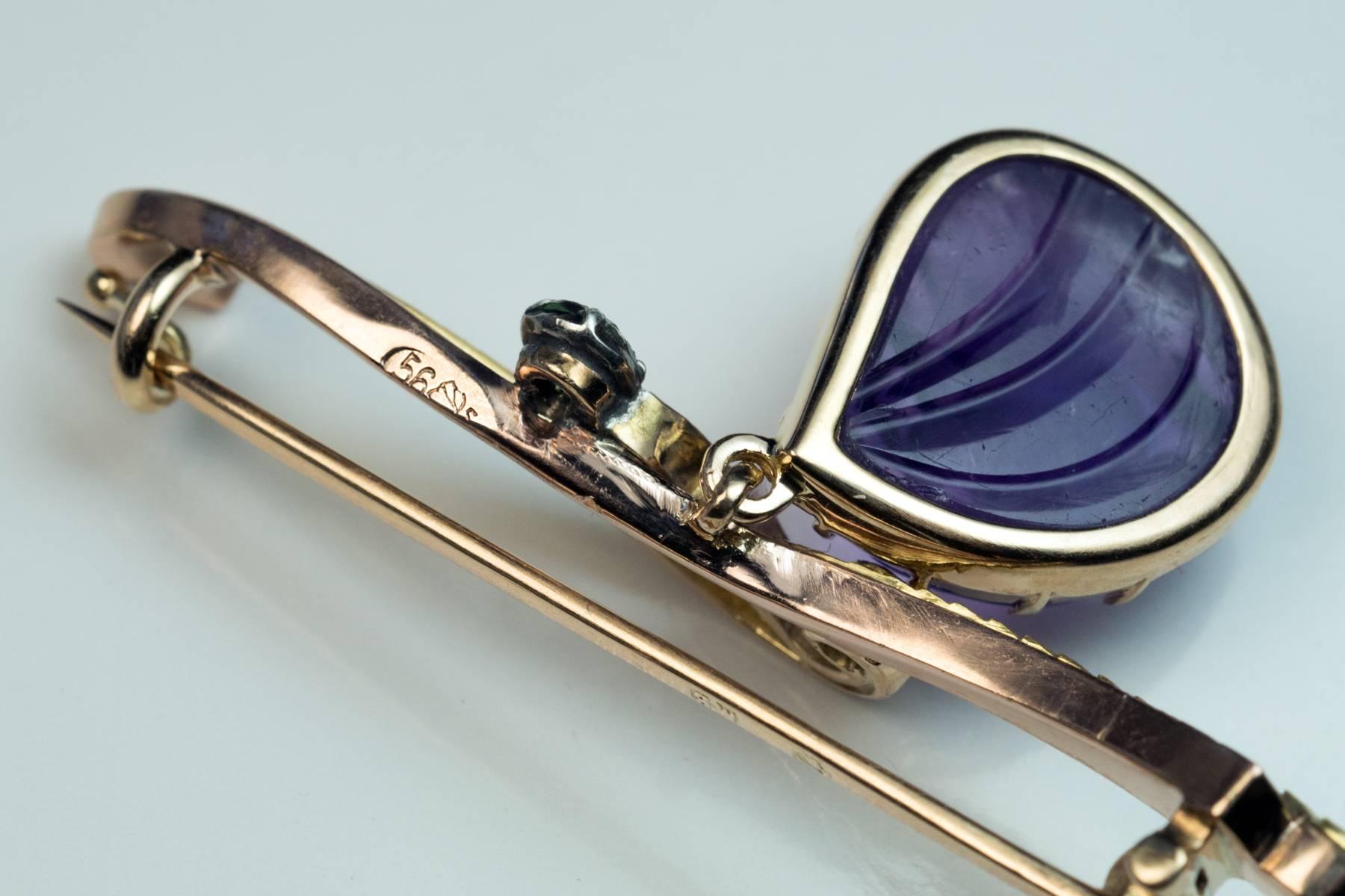 hergestellt in Moskau zwischen 1899 und 1908

Die Brosche aus 14 Karat Gold ist als stilisierter Zweig mit einem hängenden Amethyst in Lünettenfassung gestaltet und mit einem grünen Demantoid-Granat akzentuiert.

Der Amethyst ist so geschnitzt,