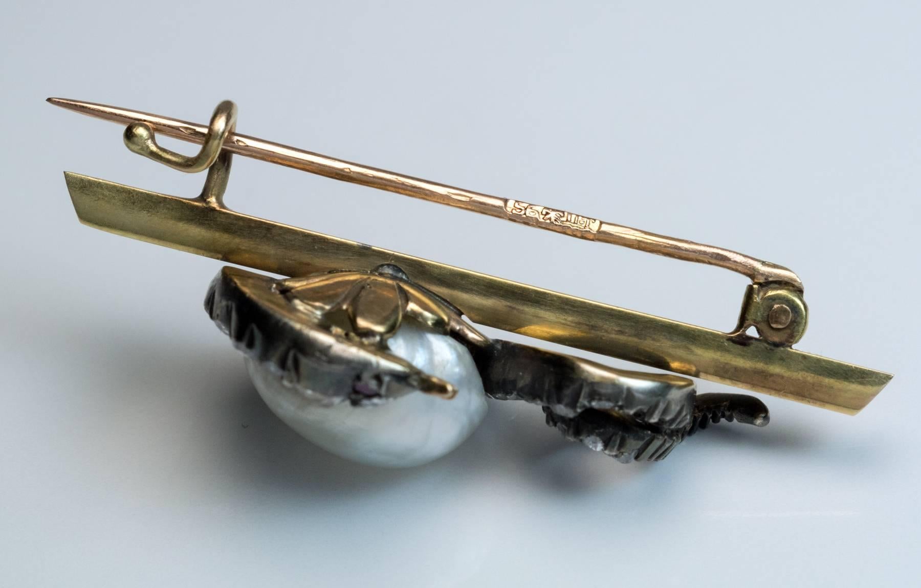 circa 1885

The brooch is designed as a diamond-set silver snake coiled around a large baroque natural pearl. The snake and pearl are mounted on a 14K gold bar.

The pearl is approximately 10.8 x 8.3 mm.

The eyes of the snake are set with red