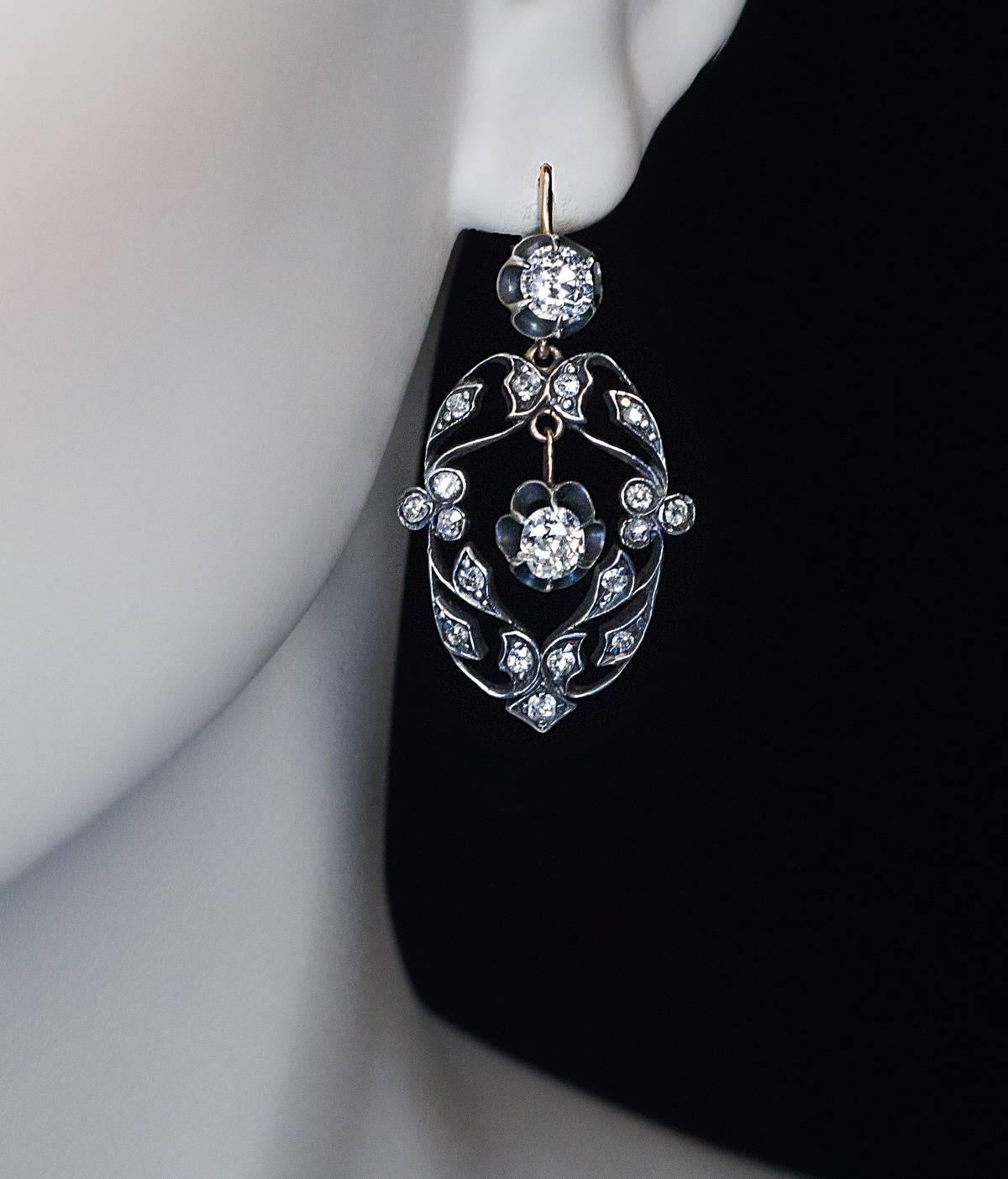 circa 1910

A pair of silver topped 14K gold earrings features 4 bright white (G color, VS1-SI1 clarity) old cushion cut diamonds (approximately 0.67 ct, 0.68 ct, 0.61 ct, 0.50 ct.) set in buttercup settings.

The ornate floral design frames are