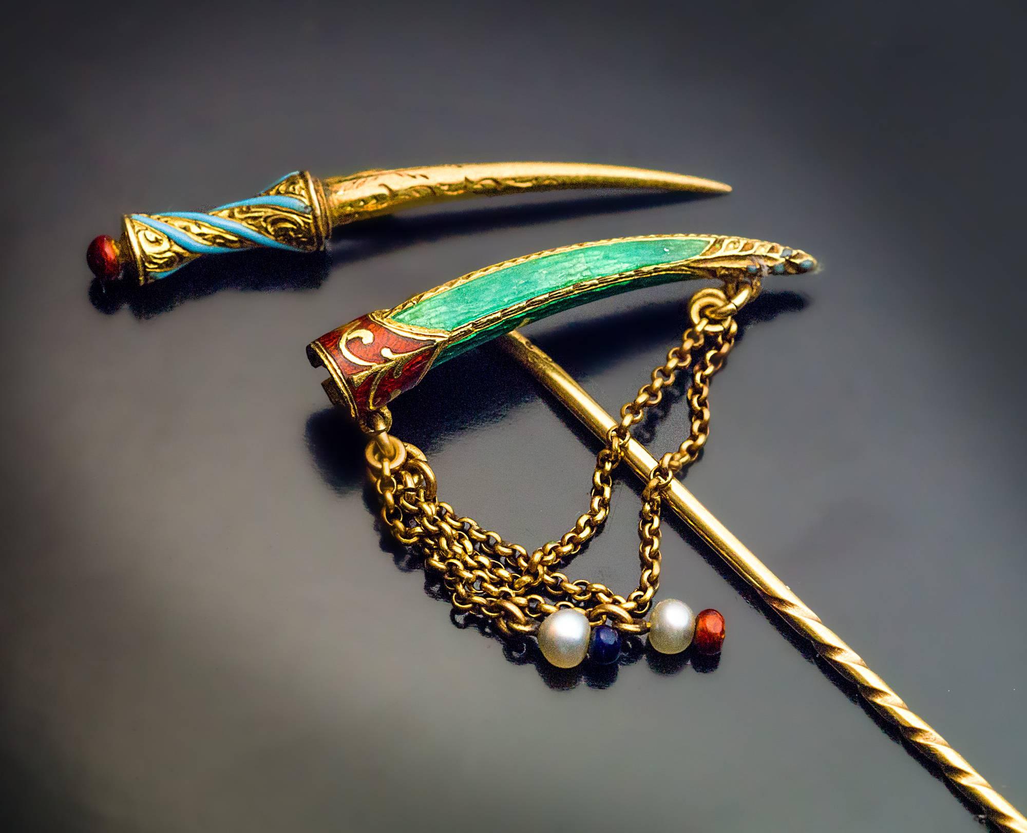 Made in the late 1870s

The 18K gold stickpin is naturalistically modeled as a miniature Turkish dagger embellished with red & green guilloche enamel, turquoise opaque enamel, pearl and enamel beads hanging on two gold chains.

It is a rare