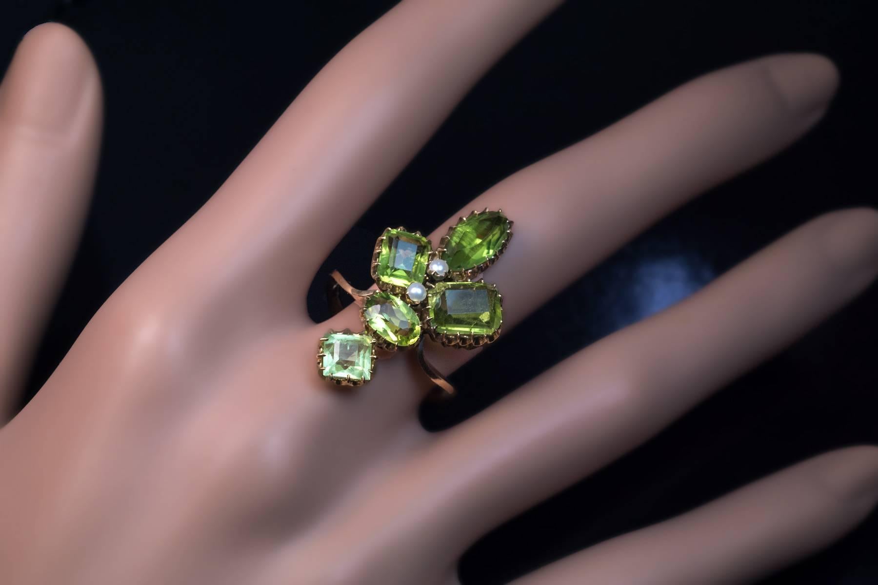 Circa 1900

An antique 14K gold ring designed as a large stylized Art Nouveau flower prong-set with five peridots of various shapes (approximately 1.45 ct, 1.43 ct, 1.09 ct, 0.94 ct,  0.75 ct and two small half pearls.

Estimated total peridot