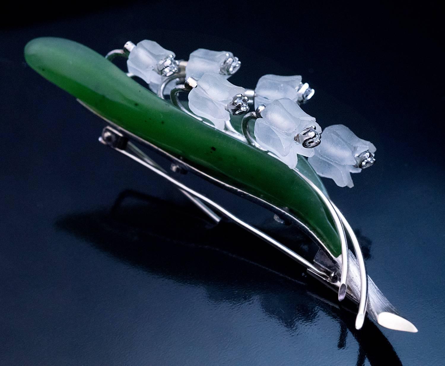 This large realistically modelled 3 – dimensional white 14K gold, hand carved nephrite jade and frosted rock crystal lily of the valley brooch / pin was made in Vienna, Austria in the 1950s.

Each flower is set with a diamond.

Marked with horse