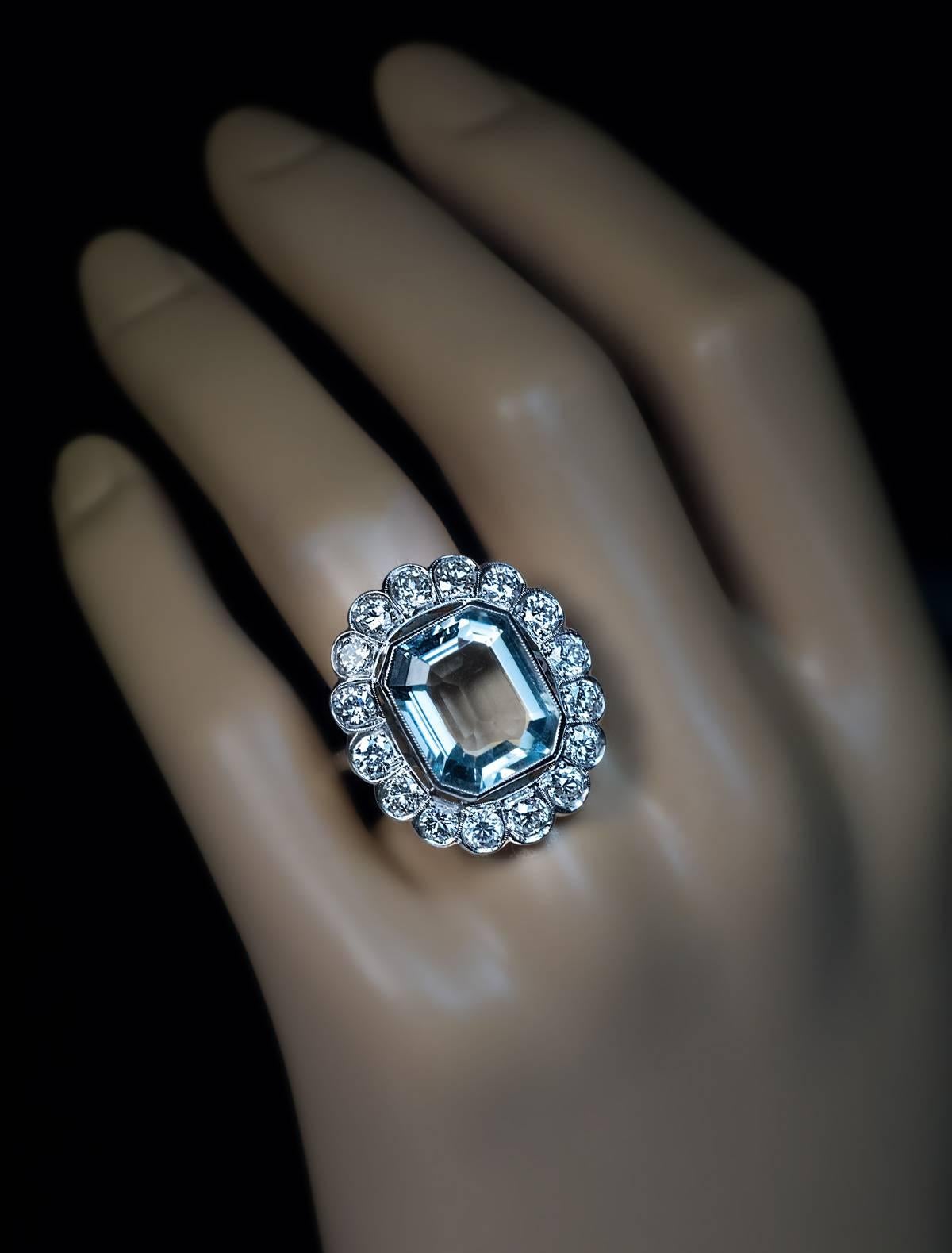 An impressive hand-crafted platinum ring from Art Deco era is centered with an emerald cut cool greenish-blue aquamarine (measuring 14.3 x 12 x 6.45 mm, approximately 7.58 ct) framed by sixteen old European and transitional cut brilliant