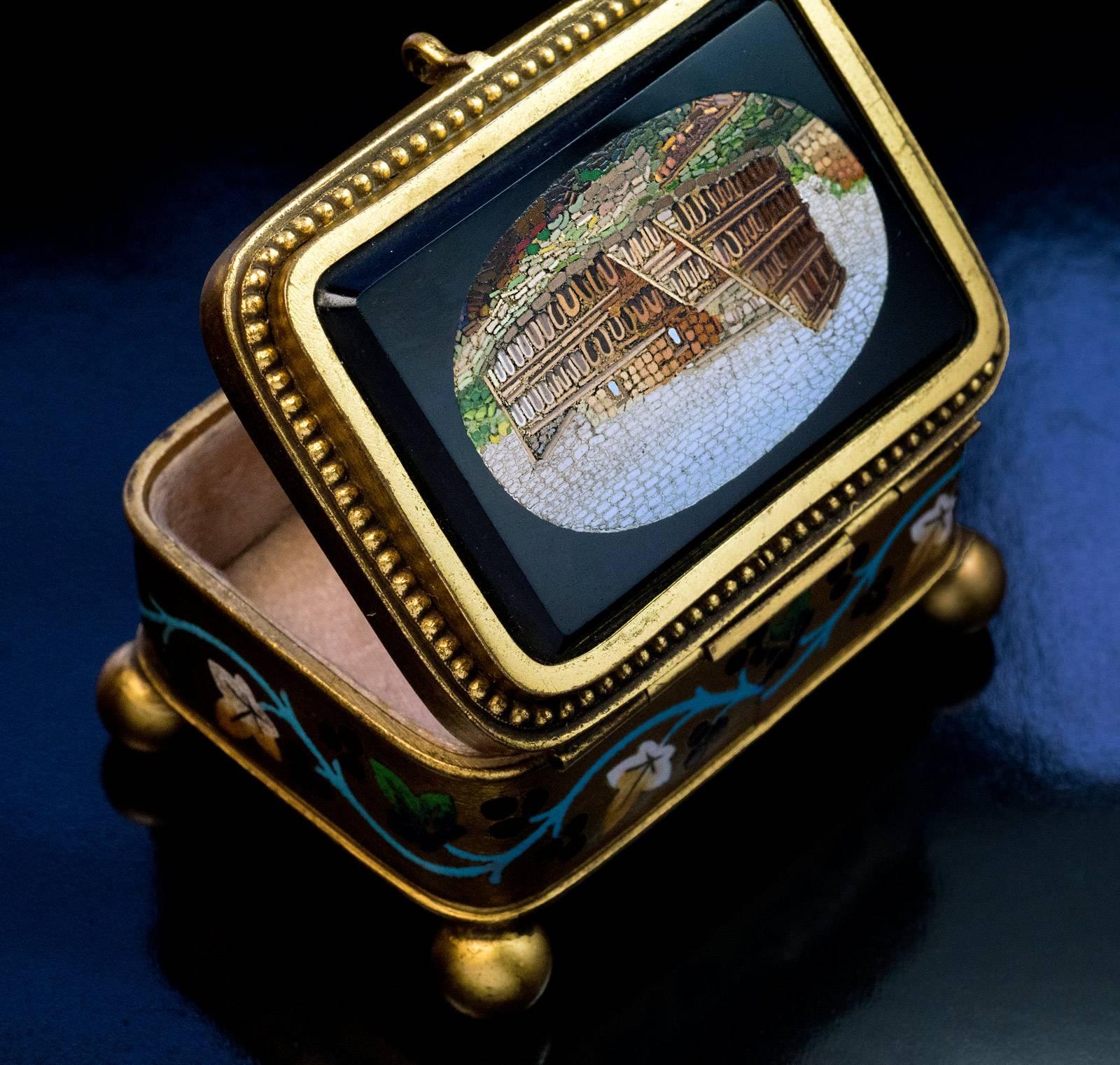 Rome, circa 1875
An antique gilded bronze jewelry box features a fine micro mosaic view of the Colosseum (Coliseum) in Rome by a prominent micro mosaic artisan Cesare Roccheggiani. The walls of the box are embellished with a champleve enamel