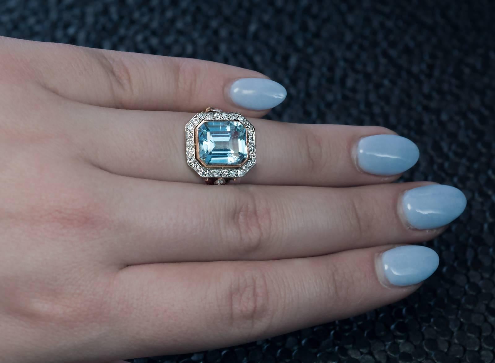 circa 1930
A 14K gold ring features an emerald cut cool blue aquamarine (measuring 11.26 x 9.80 x 6.80 mm, approximately 5.14 ct) framed by old single cut diamonds set in silver over gold and flanked by fleur-de-lis motif shoulders embellished with