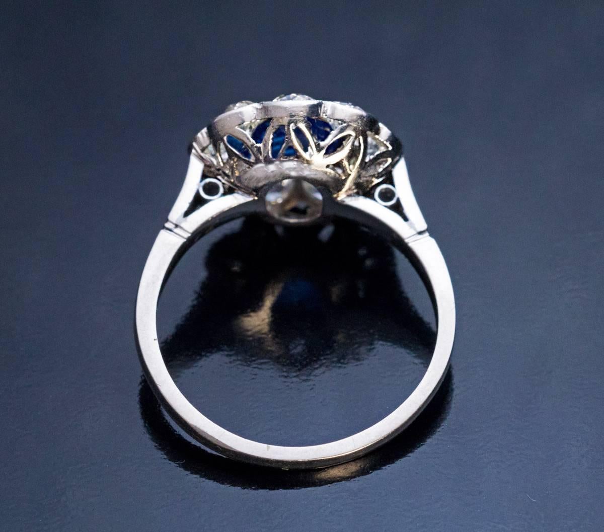 Circa 1920s
A vintage milgrain platinum engagement ring of a classic cluster design is centered with a royal blue sapphire (approximately 1 carat) surrounded by nine sparkling bright white mostly old European cut diamonds (G color, SI