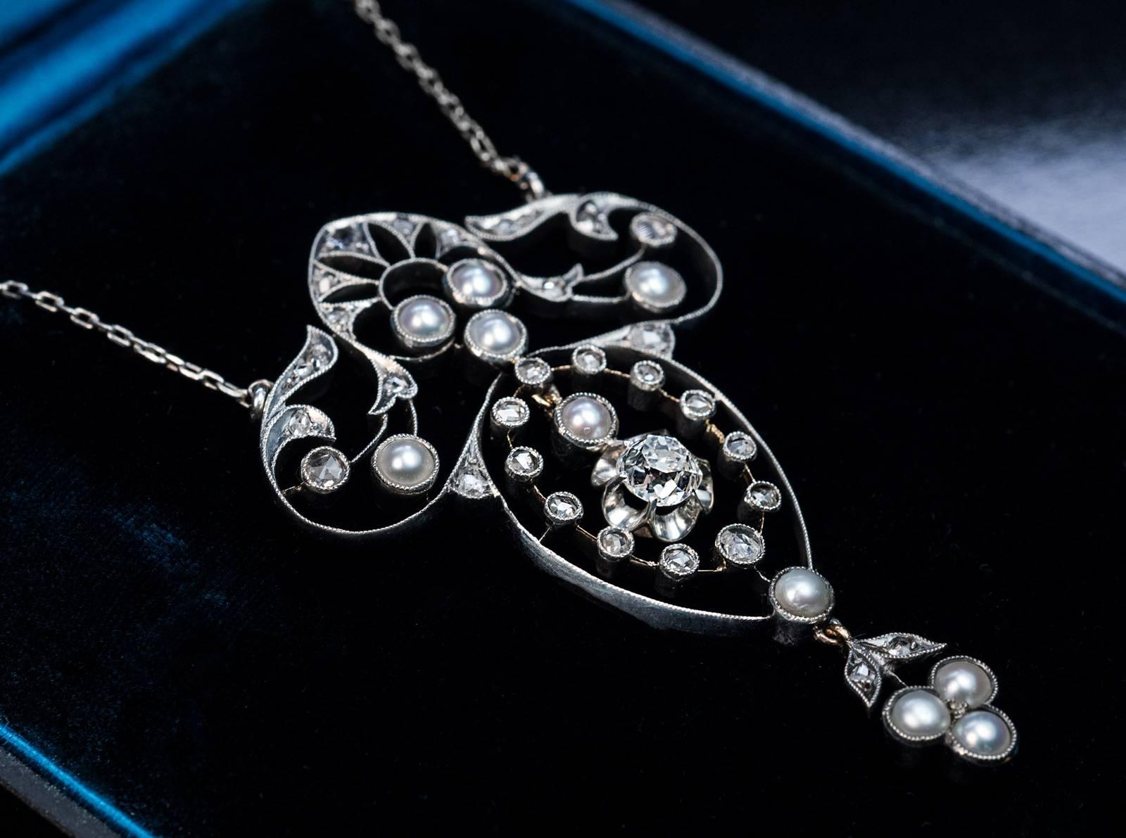 Circa 1905
An elegant antique Edwardian era pendant necklace is crafted in silver-topped gold and embellished with diamonds and half pearls. The pendant is centered with a dangling bright white old cushion cut diamond (measuring 5.1 x 5 x 3.95 mm,