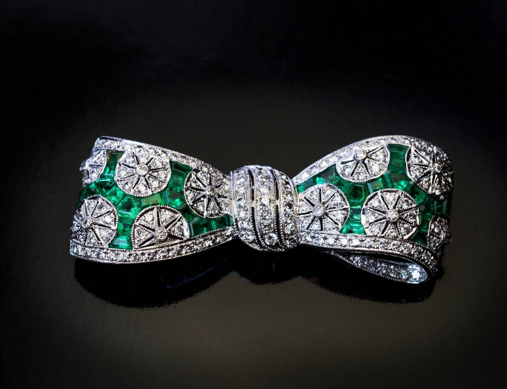 Circa 1930s
A handcrafted bow-shaped platinum brooch / pin is densely set with diamonds and calibre cut vivid green emeralds.
Estimated total diamond weight is 1 carat.
Approximate total emerald weight is 1.30 ct.
Width 46 mm (1 13/16