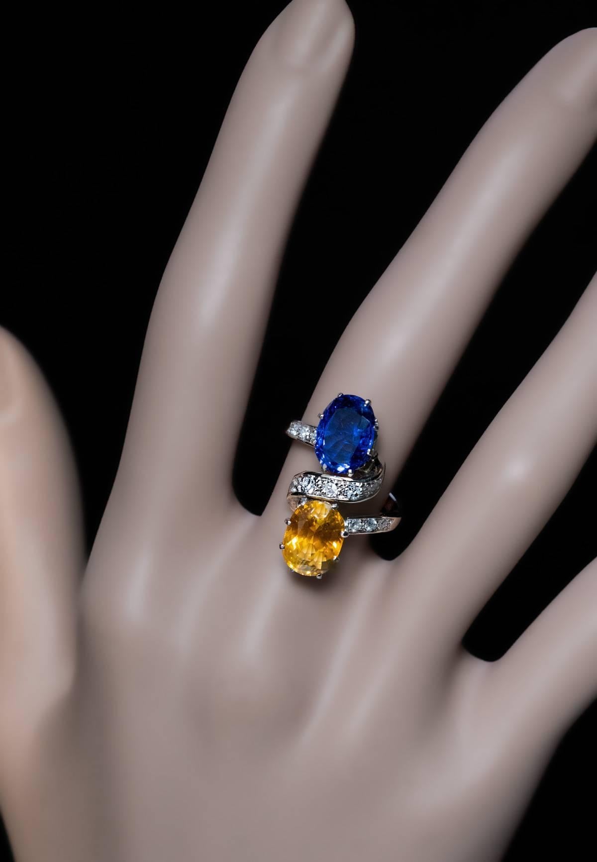 Circa 1950
A vintage French platinum and white 18K gold ring features royal blue and tangerine orange oval sapphires accented by a diamond-set stylized ribbon.
The blue sapphire measures 10 x 7.5 x 4.15 mm, approximately 2.49 ct; the orange sapphire