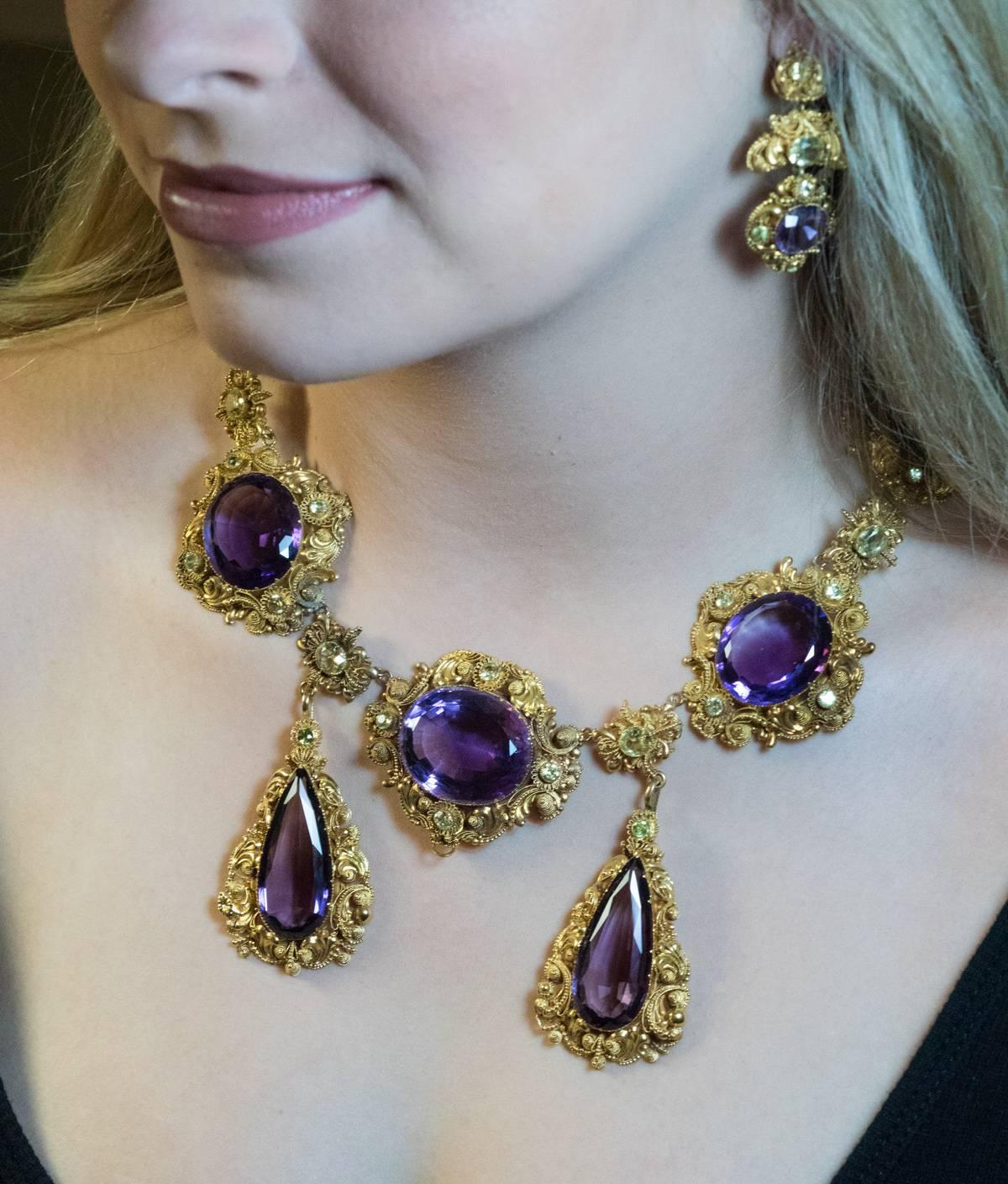 This magnificent antique parure from the late Georgian era, circa 1830, features large faceted amethysts accented by green chrysoberyls set in ornate filigree 15K gold settings.

The parure (early 19th century French name for jewelry sets) consists