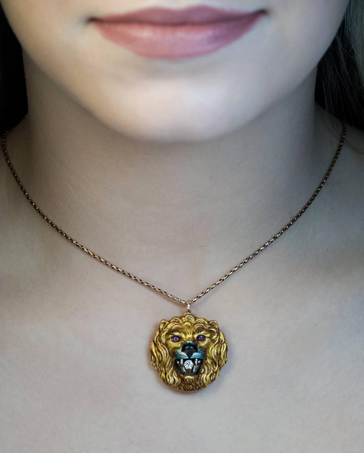 Circa 1890

An unusual antique Victorian era 14K gold pendant / brooch is superbly modeled as a lion’s head holding a diamond (approximately 0.16 ct). The eyes are set with rubies. The entire head is painted with enamel to depict the lion’s