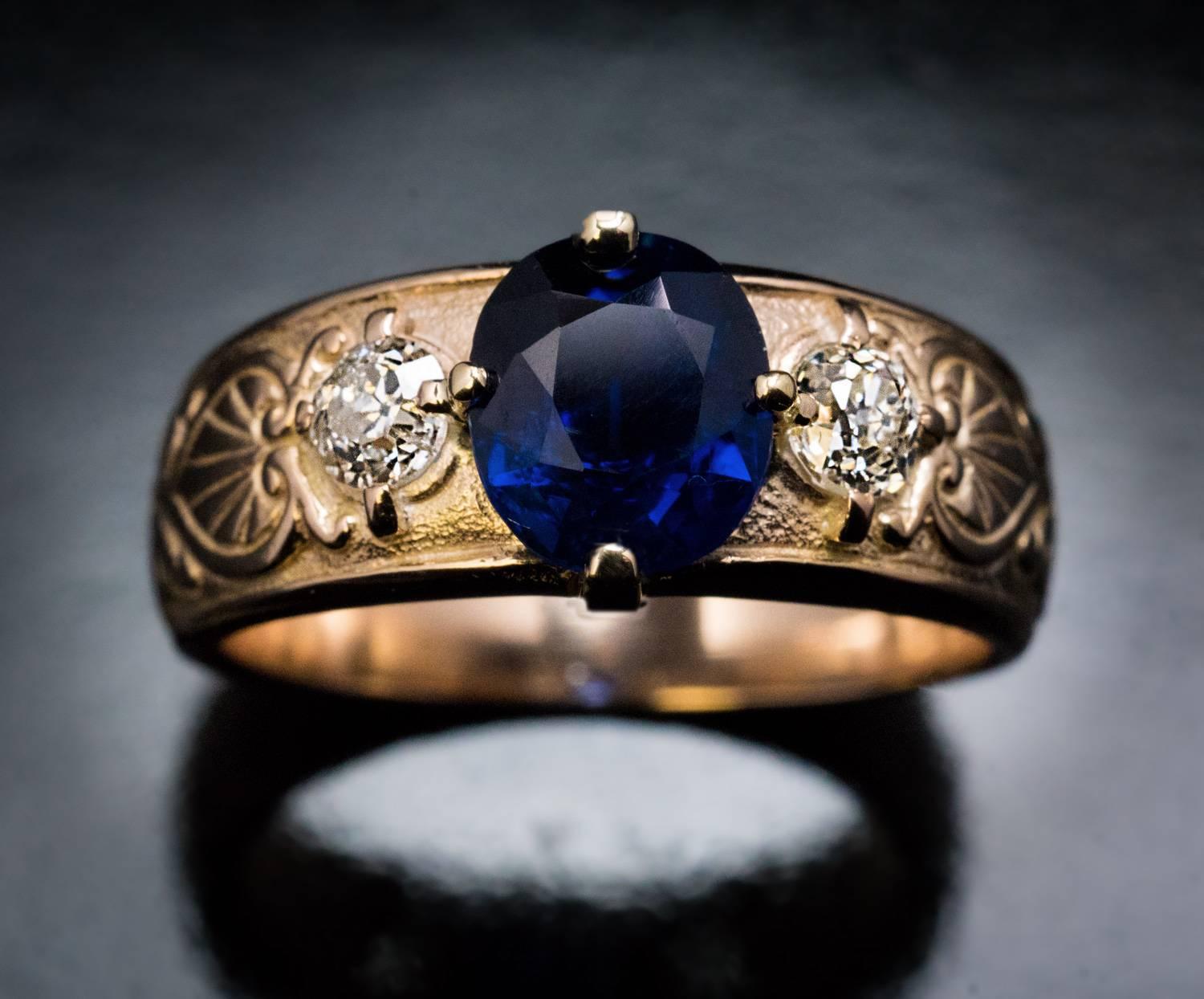 Circa 1910

An antique Russian 14K gold ring features a 1.97 ct natural sapphire of a deep royal blue color. The sapphire is flanked by two chunky old mine cut diamonds (approximately 0.24 ct and 0.22 ct). The sides of the ring are carved with