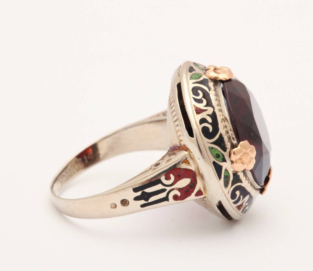 An generous 6.4 kt faceted garnet, surrounded by polychrome symbols. is set in 14kt white and rose gold for a visual treat. The dramatic color palette surrounding the garnet is brick red, forest green and black in forms that suggest a floral motif.