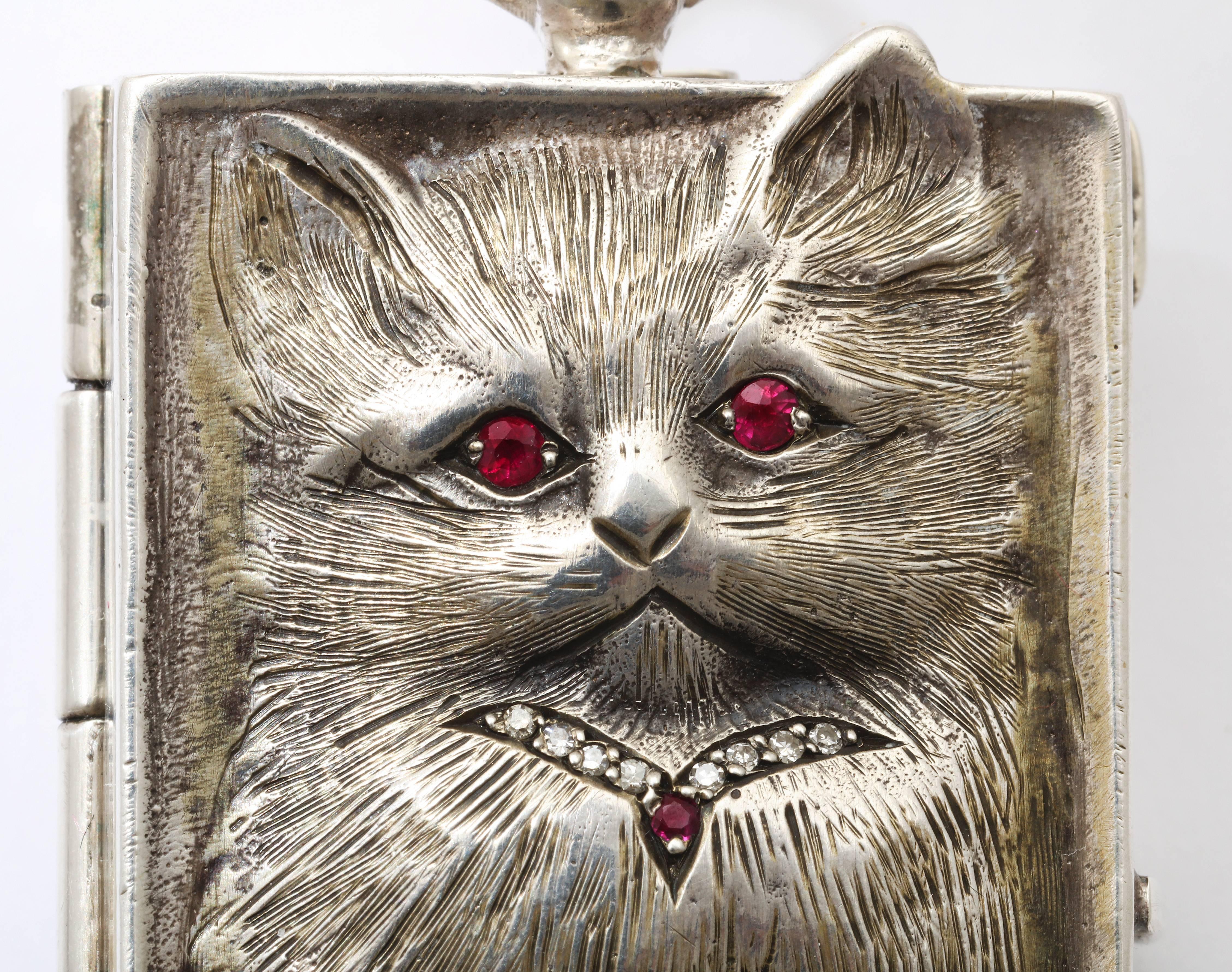  A two  inch cat pendant is sterling silver, has ruby eyes and a diamond collar, and is sweet enough to hug. Engraved on both sides en repousse, this feline is jumping from its confines. The giggle comes when you turn it over and see the diamond
