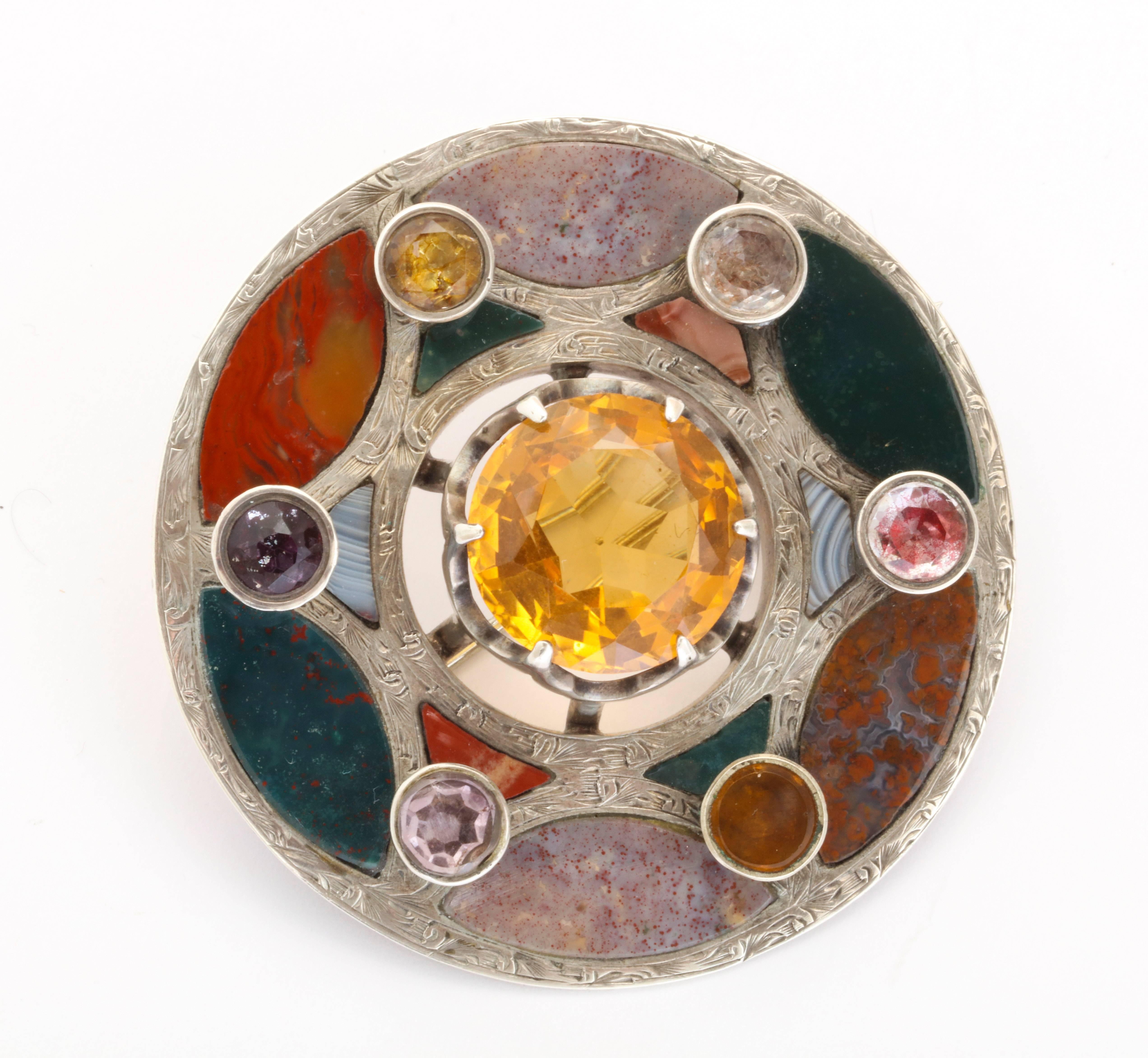 A Victorian Scottish Brooch flashes the stone cutter's  mastery in setting moss agate, jasper, montrose agate and bloodstone into a star of silver. The silver is engraved at the border and at the star. Amethyst, Citrine and Garnet heighten the