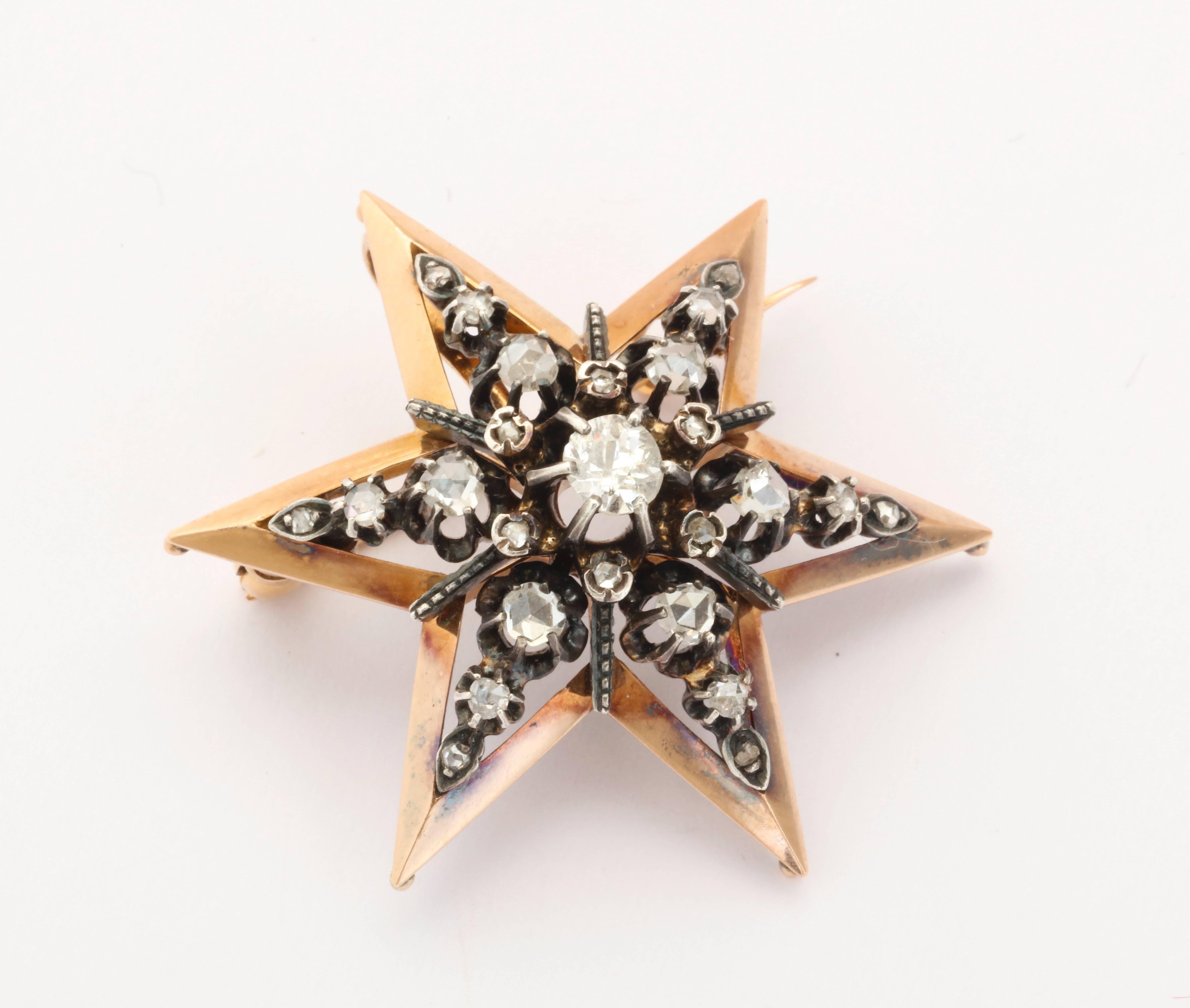 A star pendant or brooch boasts a central off round diamond sitting nestled in a cluster of rose cut stones. The diamonds sit forward in the 15 kt yellow gold frame, that has just a hint of rose tone, giving contrast and enhancing the white of the