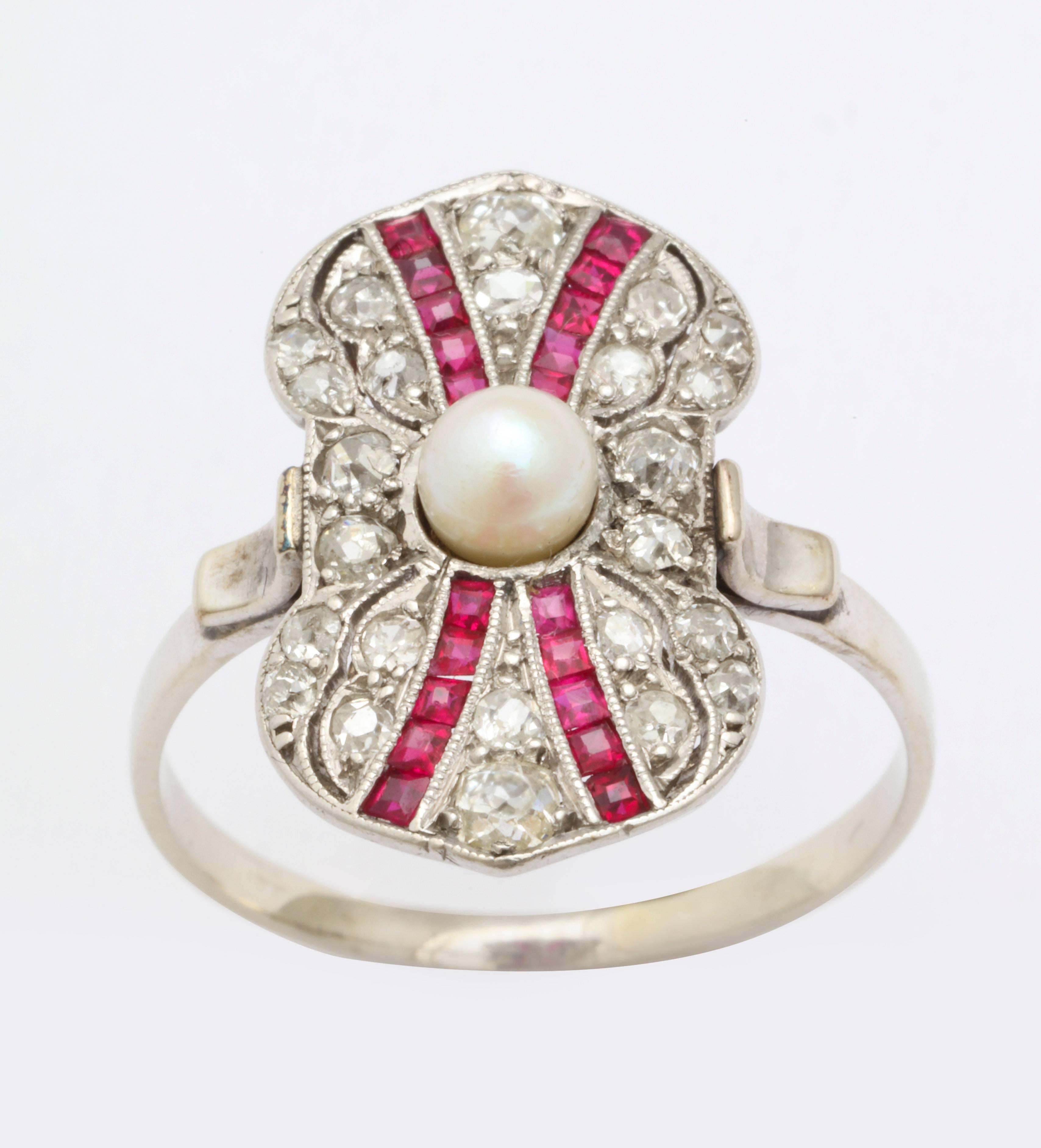 A ring that is a celebration of Art Deco color, form and geometry brings you converging rows of rubies on a background of diamonds, brought together with a central pearl. The outer form is an unusual, irregular bow that is gracefully pinched in the