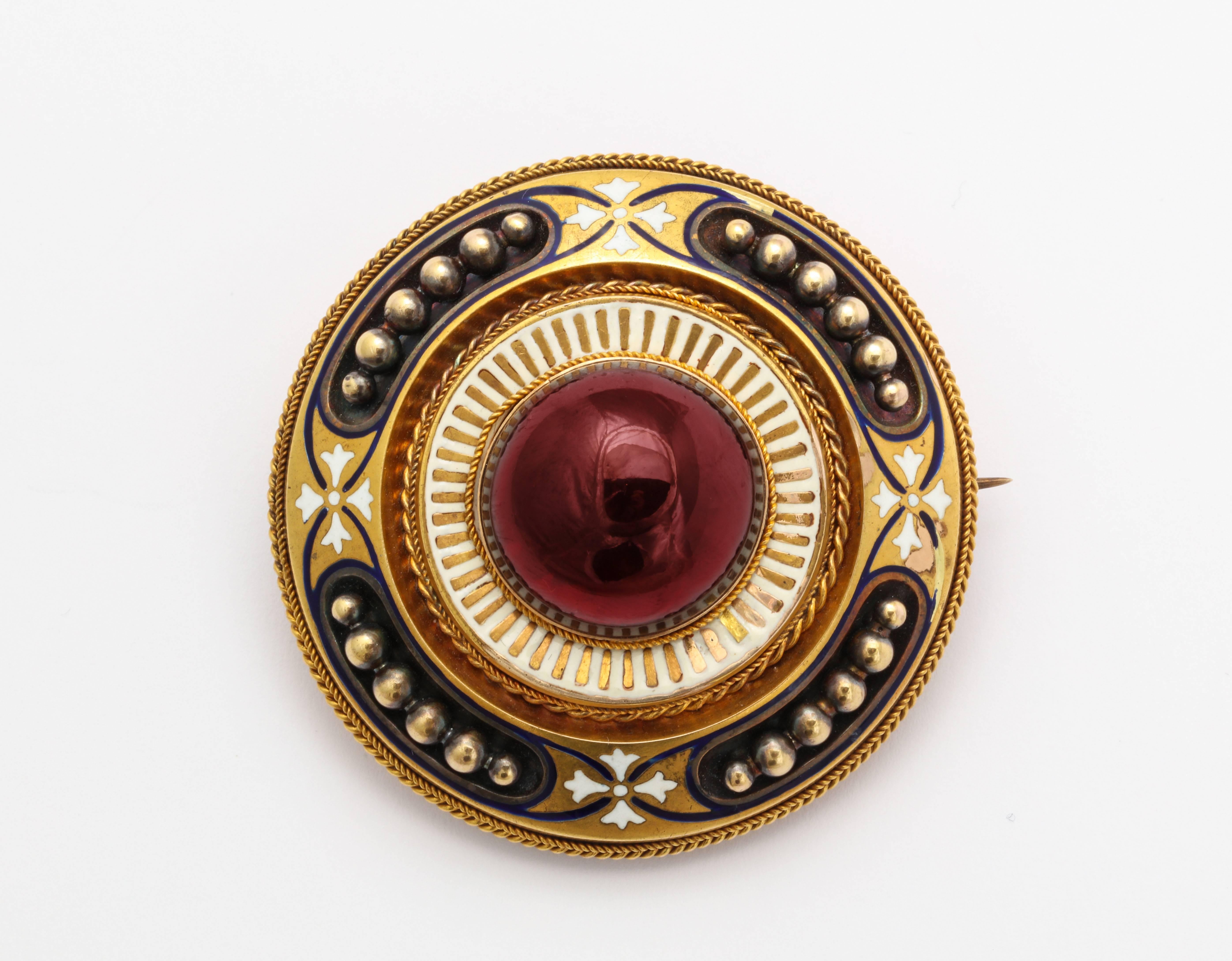 A superb brooch of museum quality is brilliant with a glowing cabochon garnet surrounded by white and gold enamel and a locket in the back. The gold rays light the center and push the garnet to the fore. The brooch measures 2 inches in diameter. All