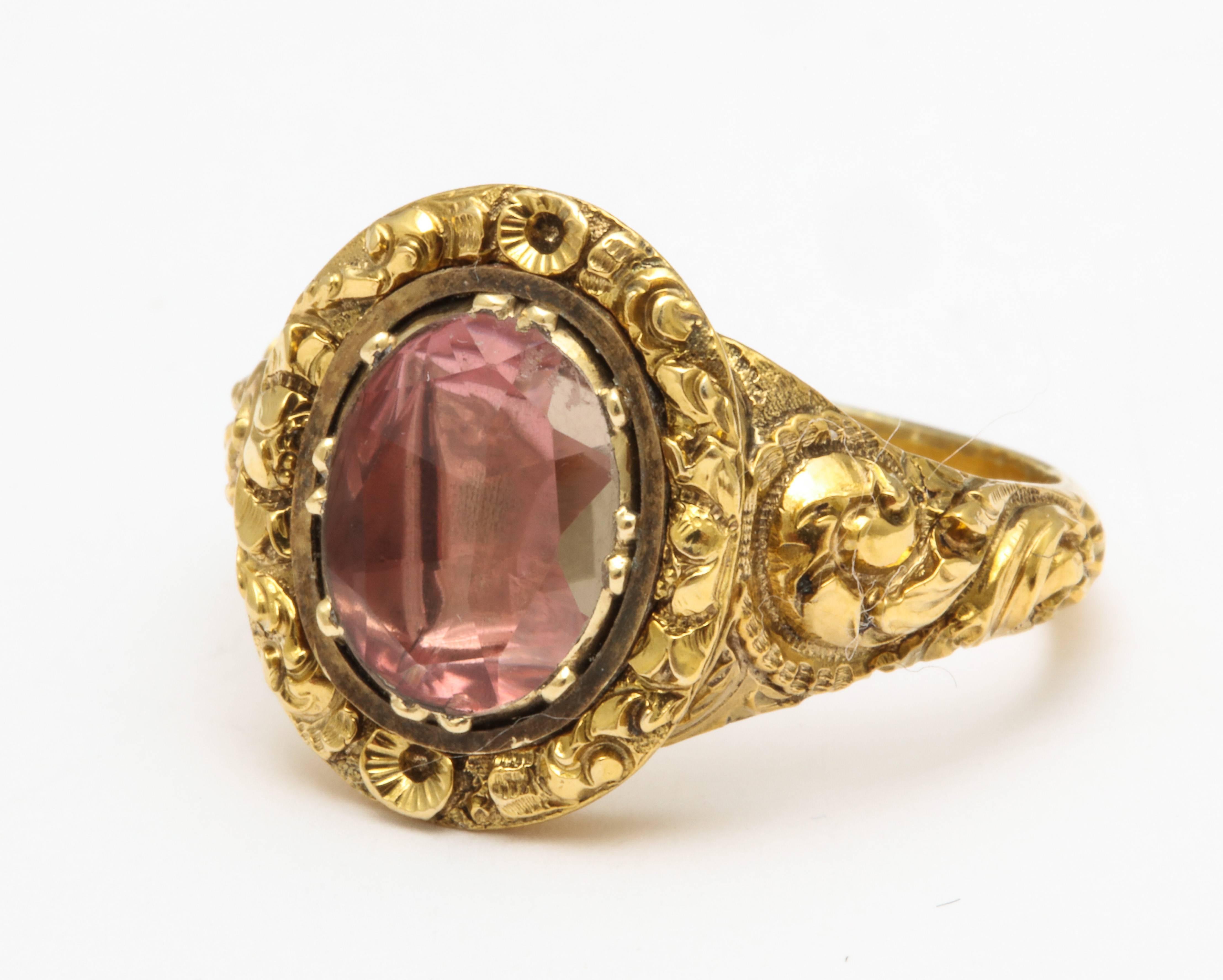 As if the pink crystal were dropped in a garden, it rests among deeply engraved and chased flowers and foliate motifs in a 15kt gold, vibrant, pink foiled Georgian setting c. 1820. The ring has a lush presence as the chasing is generous and well