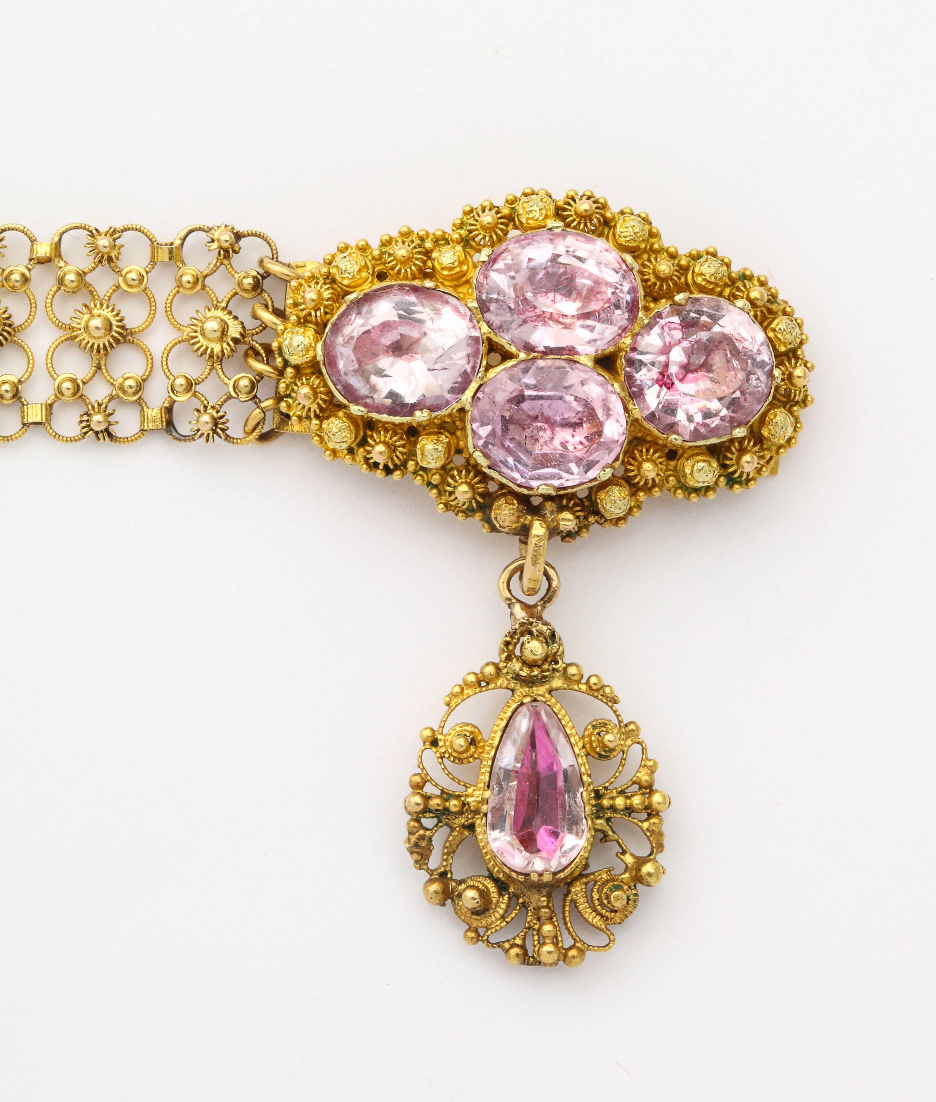 A lace like and perfect, flexible bracelet c.1830 is clasped by a plaque set with four oval pink topaz gems. Suspended is an oval of lace holding a teardrop of pink topaz. Total weight of the stones is 6 cts. All gems are closed back and foiled as