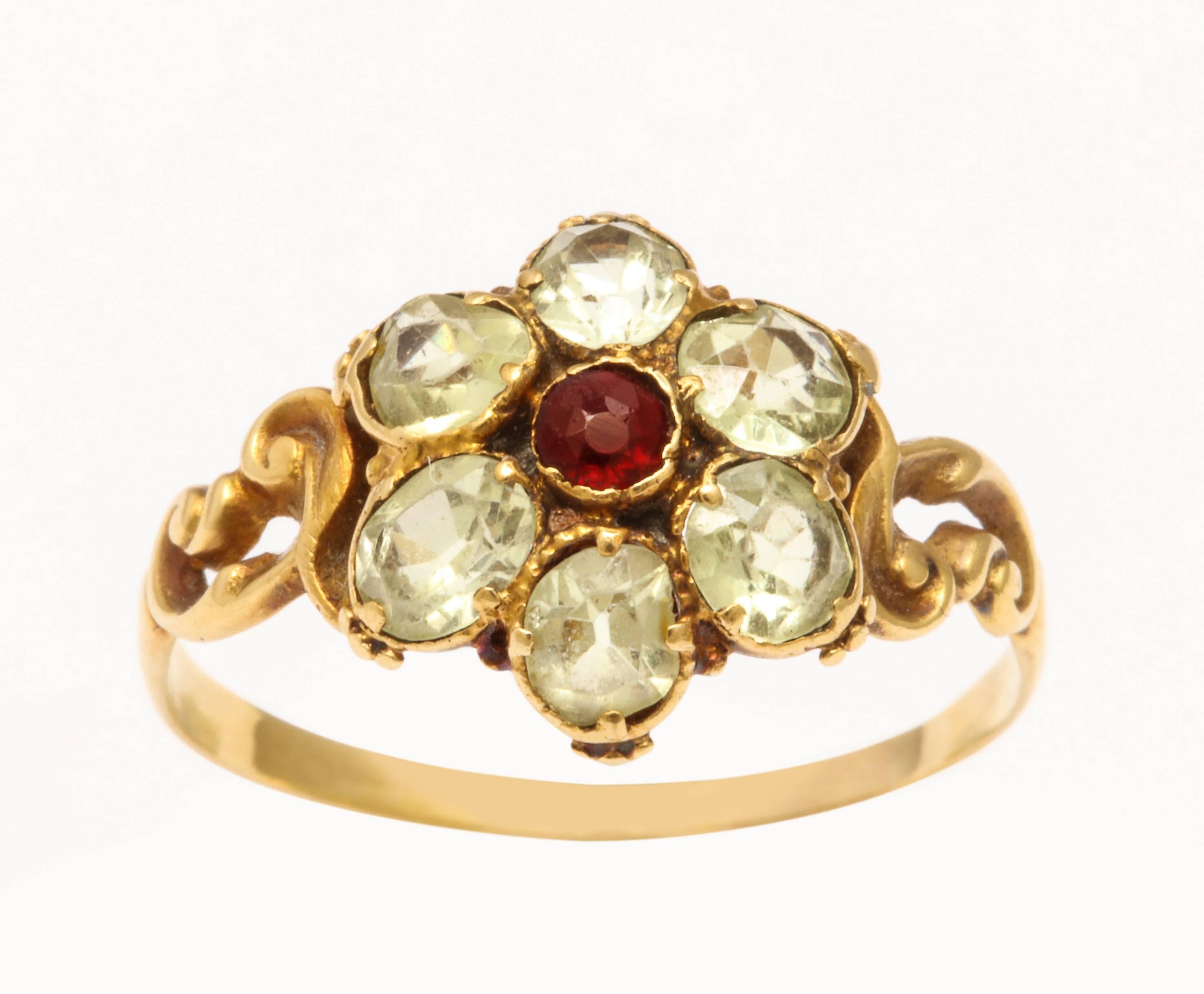 Mesmerizing, the cat's eye color of chrysolite is here set in a delicate flower in 15 kt gold with a garnet center. The stones, other than the garnet are set with open backs so that the light that enters increasing the beautiful apple green color.